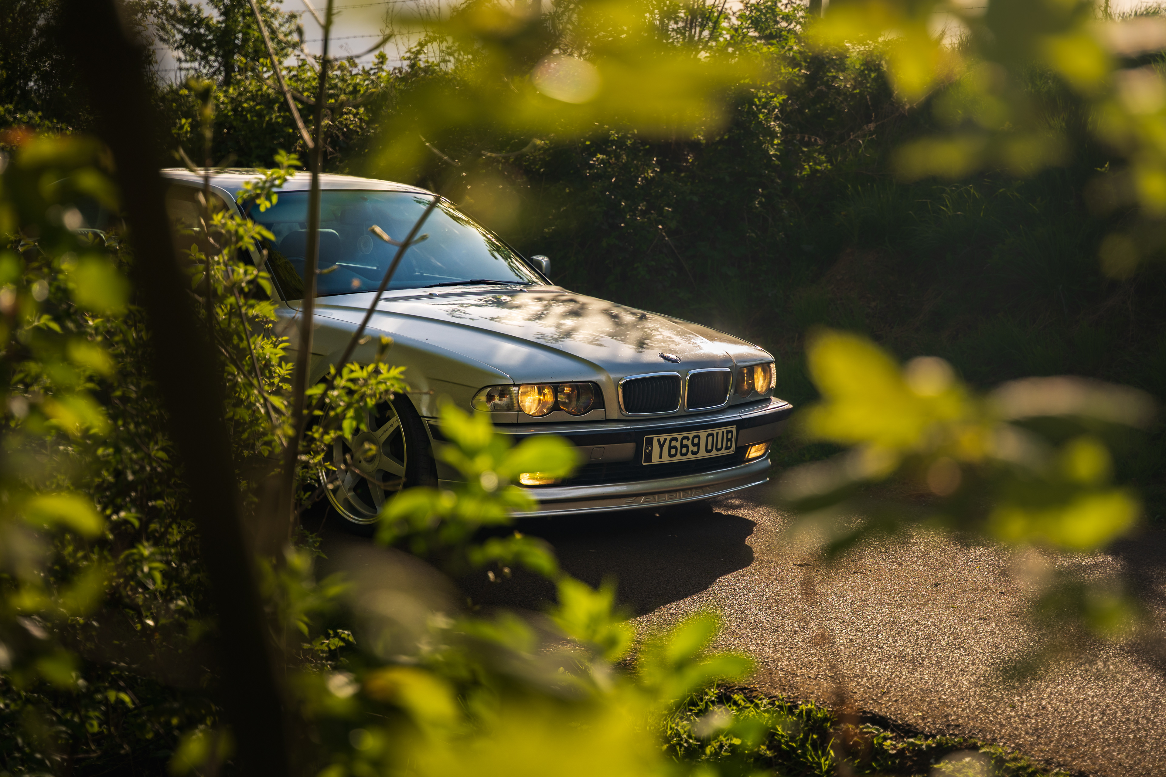 BMW 7 series e38 car partially framed through trees with cinematic depth of field