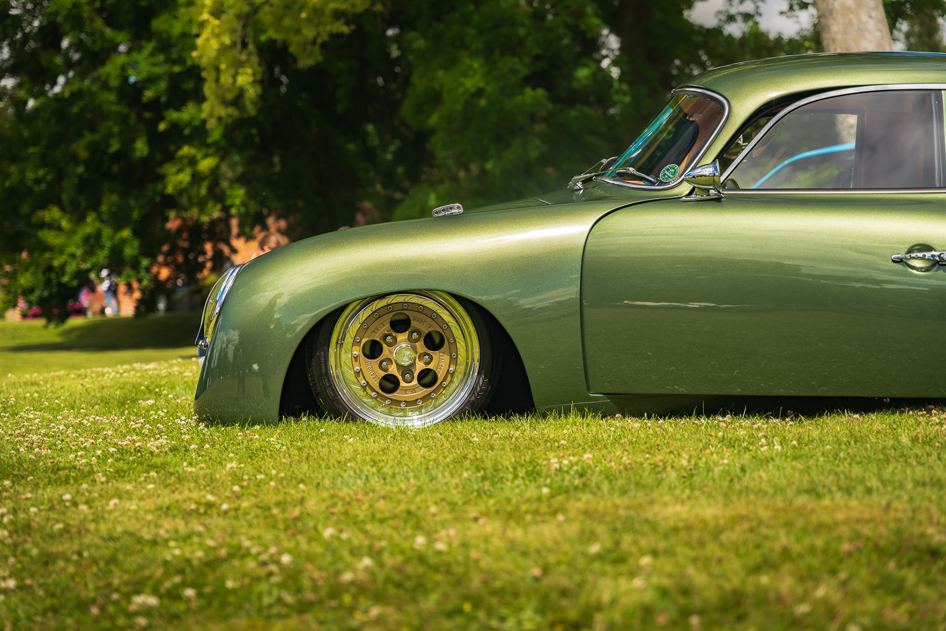 Close-up of green car Porsche Outlaw 356 front wheel and lowered suspension on grass