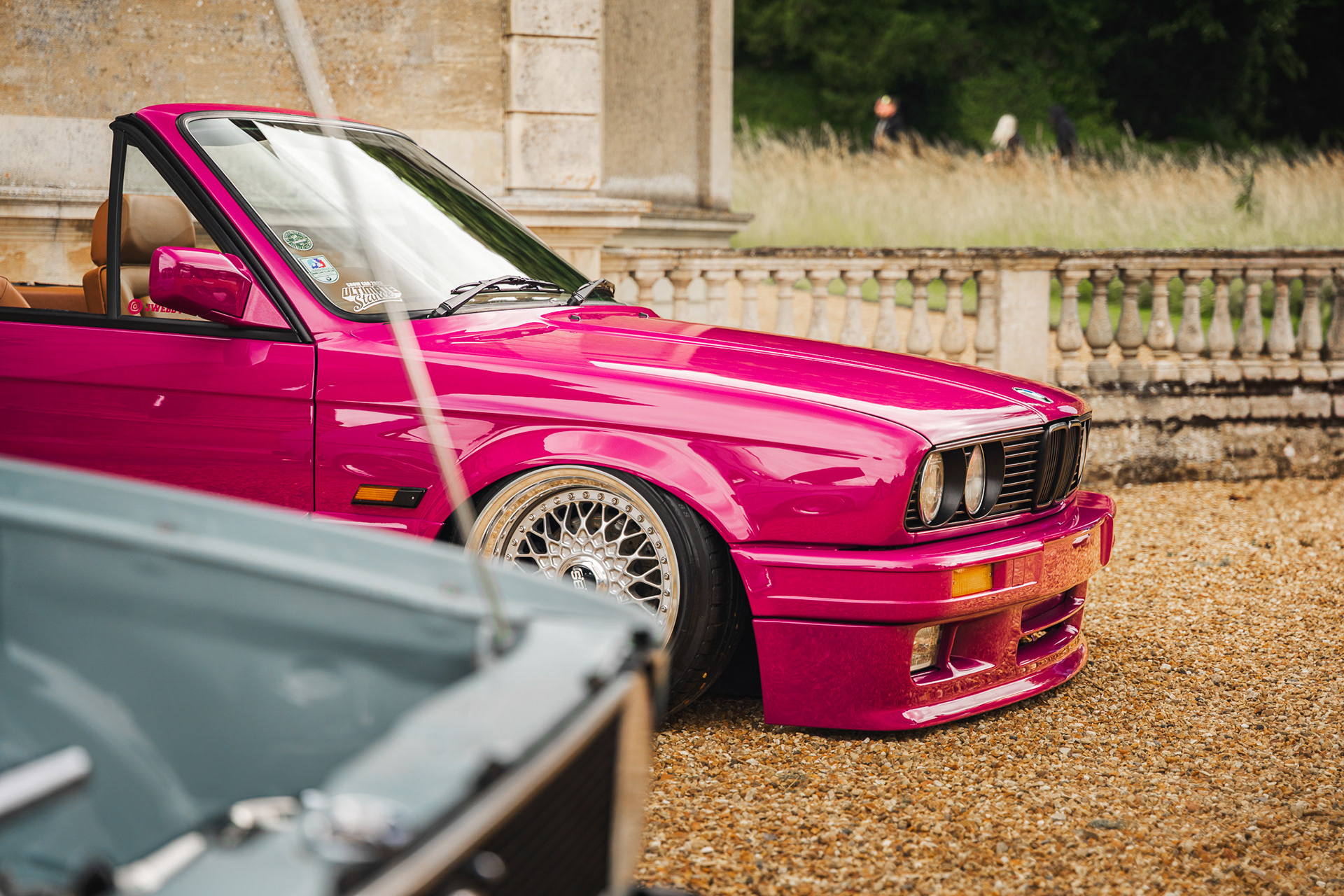 Three-quarter view of pink BMW e30 with custom BBS wheels and lowered stance