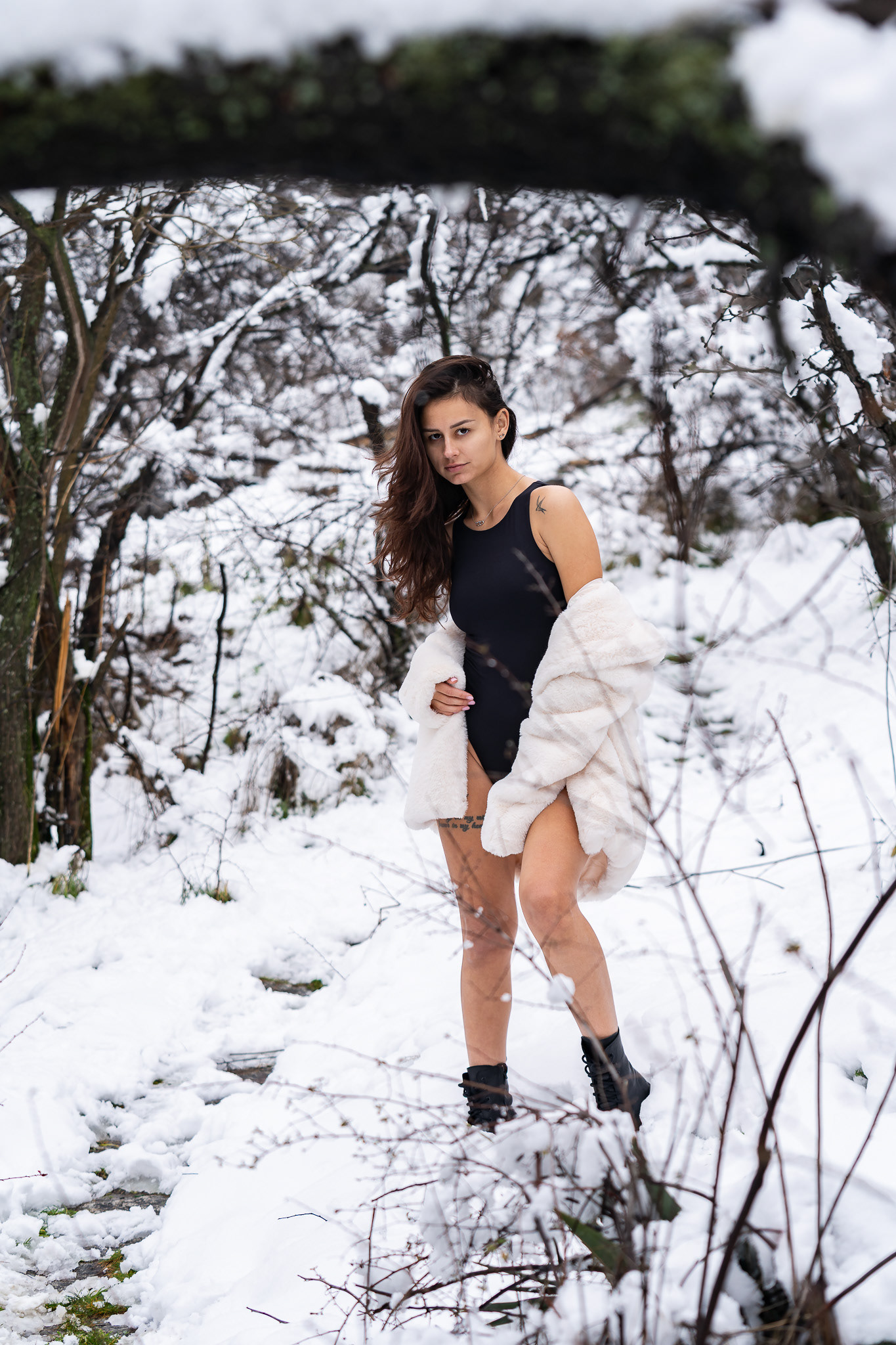 Full length winter fashion editorial of a model in a black bodysuit and white fur coat standing on a snow-covered hillside. Photography by Tenyo Barbolski, Cambridgeshire.