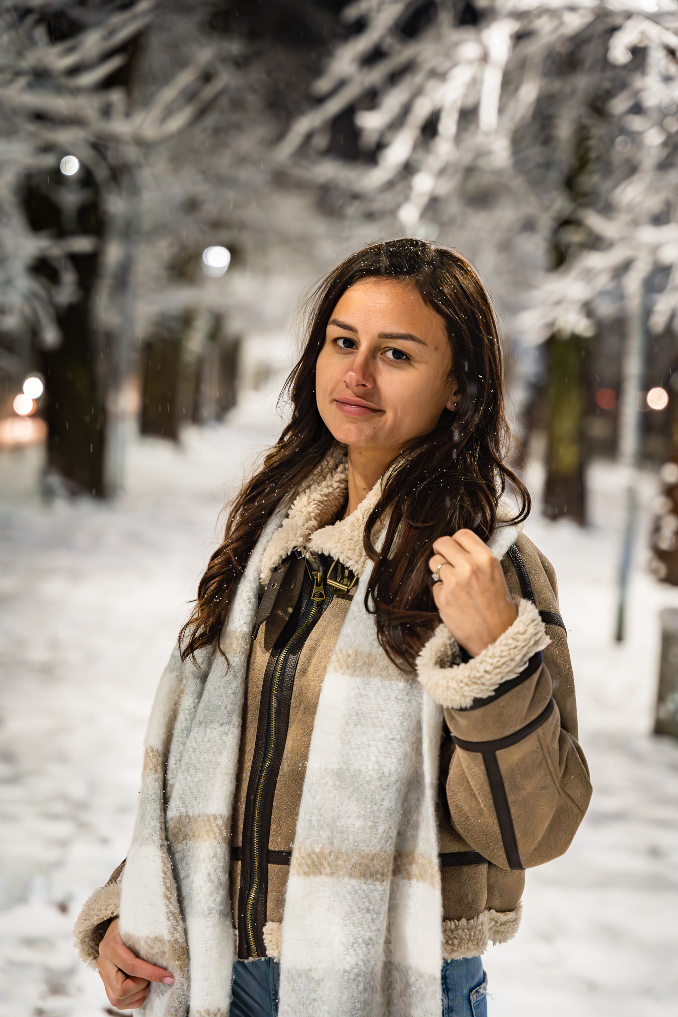 Candid evening fashion portrait of a brunette model in a shearling coat on a snow-covered street. Natural expression lifestyle photography by Arcane Media, Cambridgeshire.