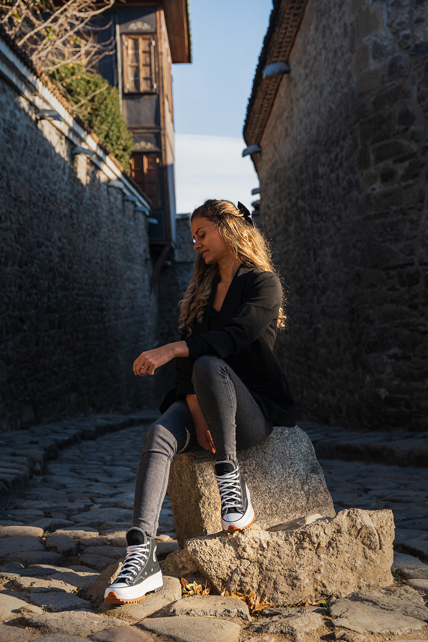 Moody lifestyle portrait in a cobblestone alley, utilizing low-angle perspective to emphasize the height of the architecture and the model's urban styling