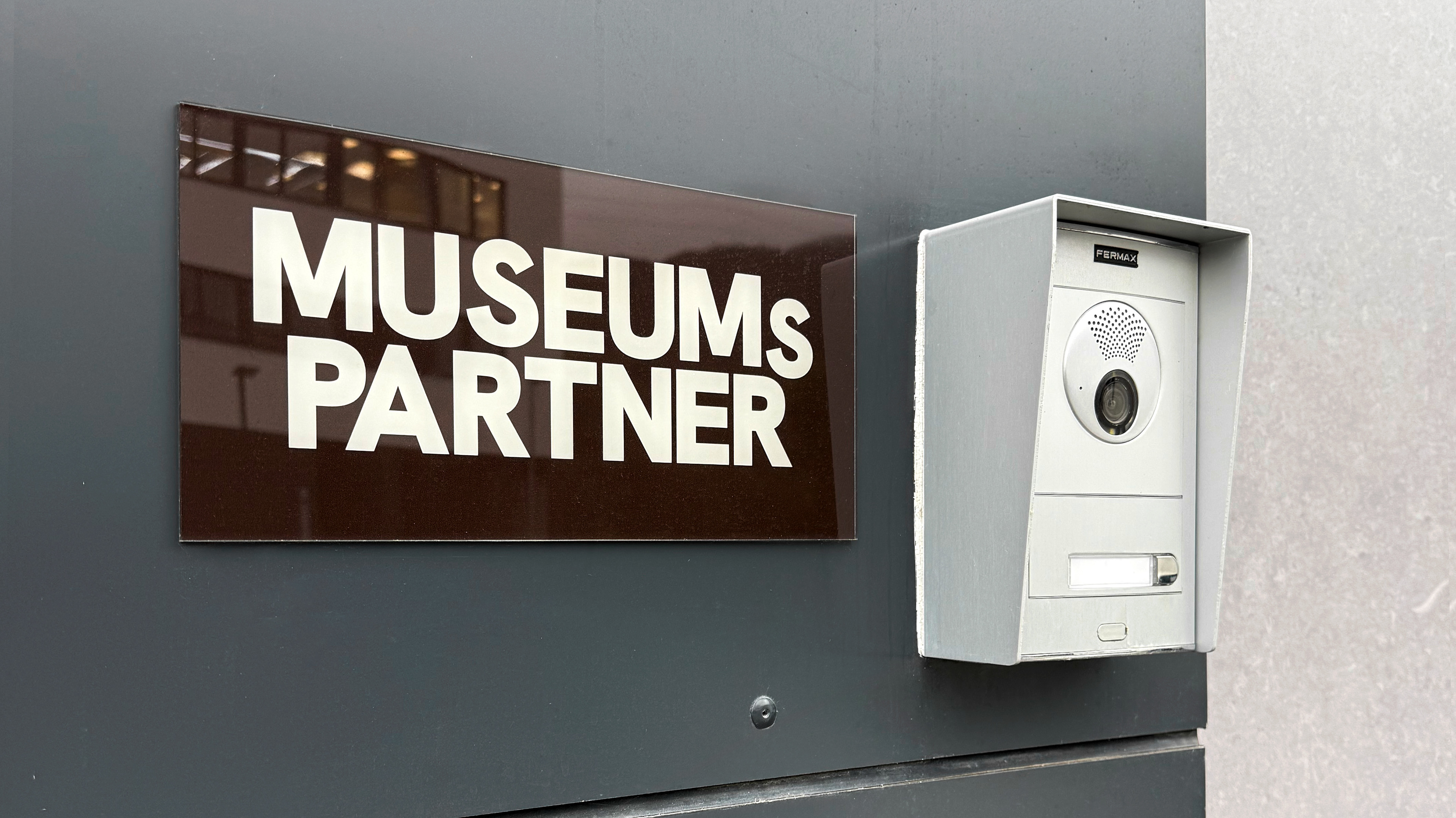 Minimalist exterior company sign for Museumspartner, demonstrating the seamless transition of the visual identity from digital platforms to physical office signage.