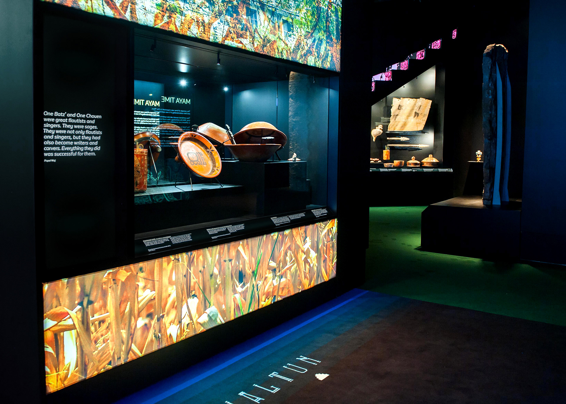 Immersive museum gallery for the Maya exhibition, featuring backlit fabric graphics and glowing Plexi panels that create a vibrant, jewel-toned atmosphere.