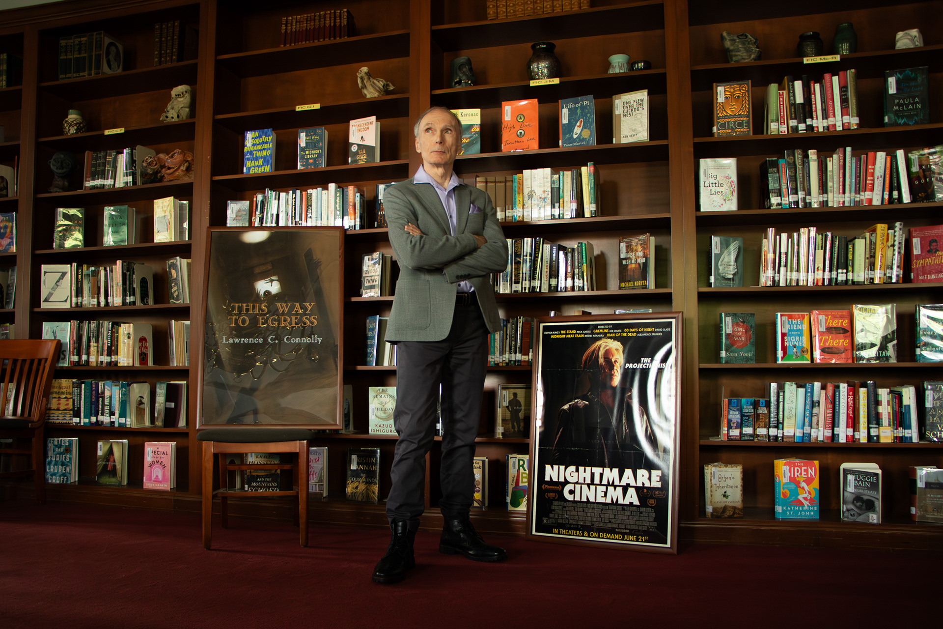 Photographed at the Sewickley Academy Library.  The poster on the left is the cover for his short story collection "This Way to Egress" Cover by Jason Zerrillo. The poster on the right is The Projectionist cover for Nightmare Cinema. "Five strangers converge at a haunted movie theater owned by The Projectionist (Mickey Rourke). Once inside, the audience members witness a series of screenings showing them their deepest fears and darkest secrets." Featuring the critically-acclaimed segment “This Way to Egress” Based on the story “Traumatic Descent” byLawrence C. Connolly. Screenplay by David Slade & Lawrence C. Connolly. Directed by David Slade. (https://lawrencecconnolly.com/stage-and-screen/)