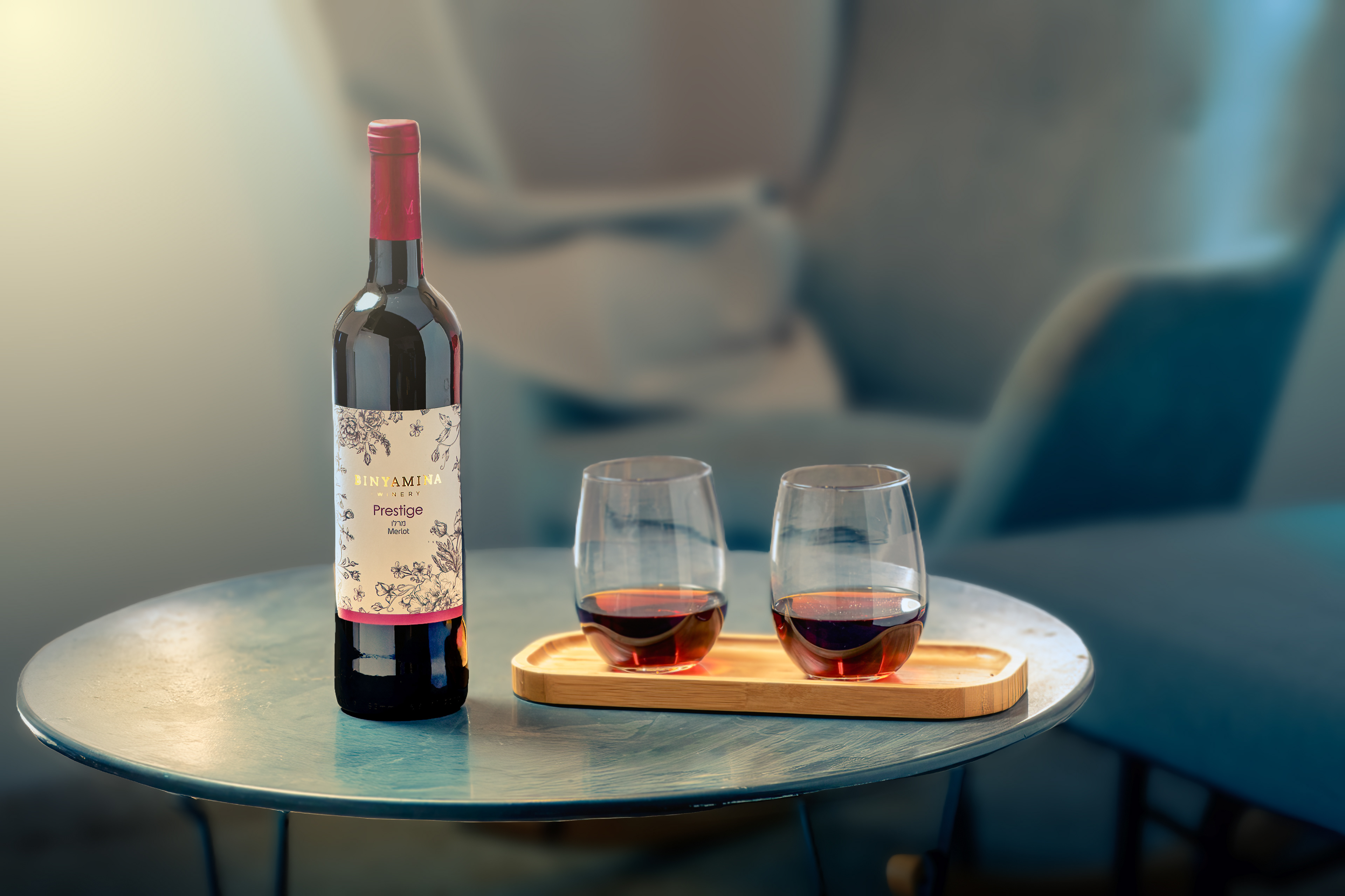 Binyamina Red whine bottle with two glasses of wine from it. In a living room with a window light and reflections on the table.