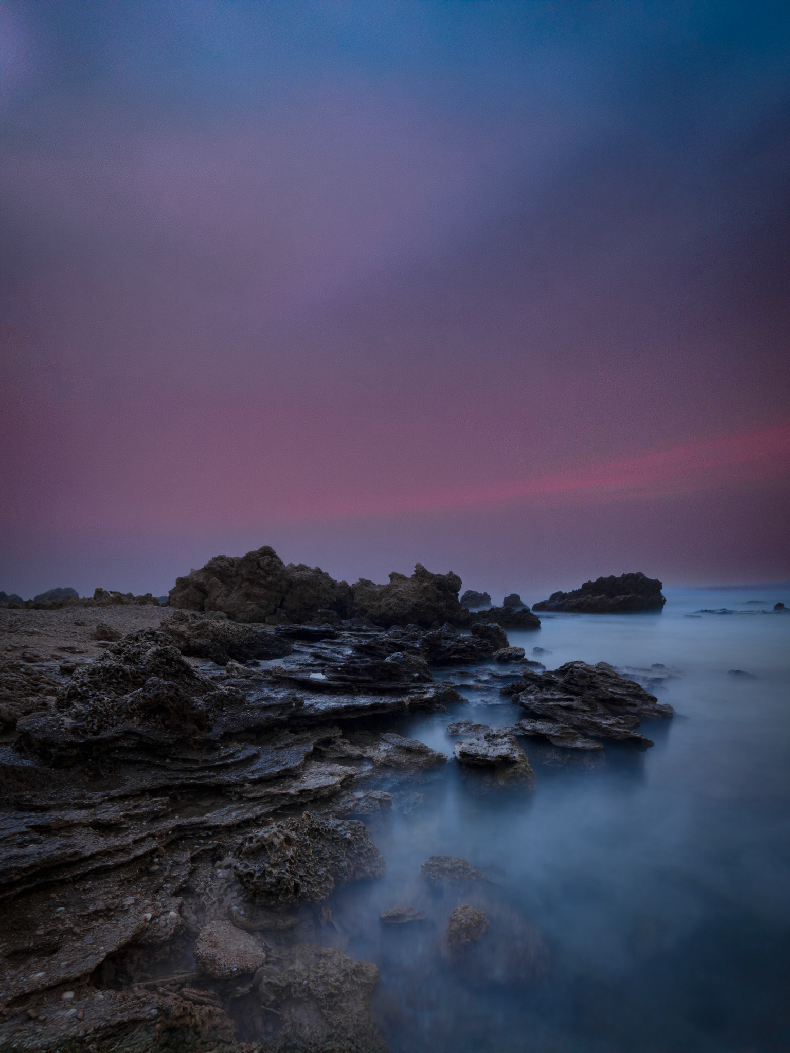 Pink sky at blue hour above a calm Mediterranean seascape and edgy rocks