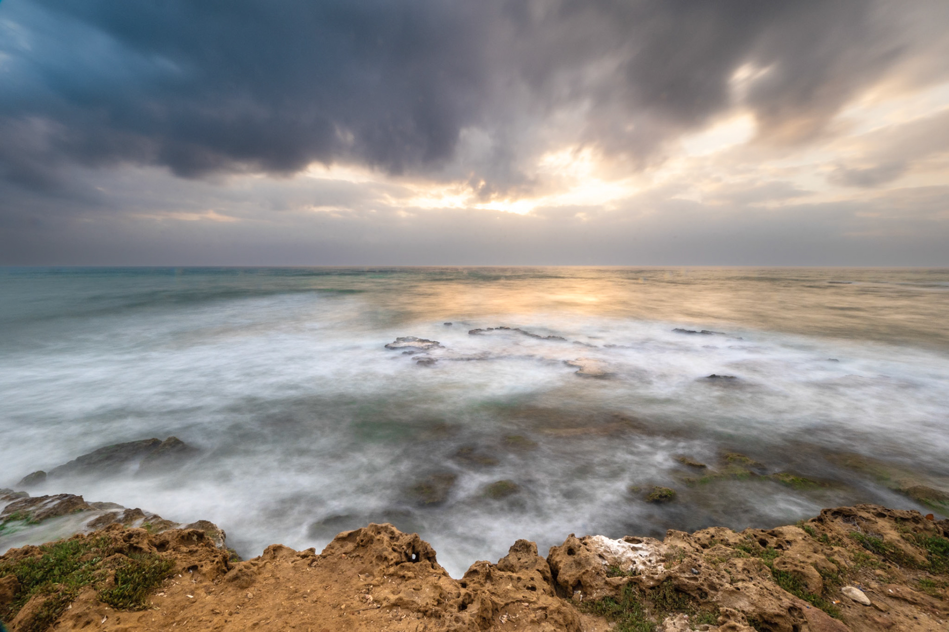 Long exposure over the sea with rocks bumping out and the shore line. Clouds in the sky and the sun setting down 