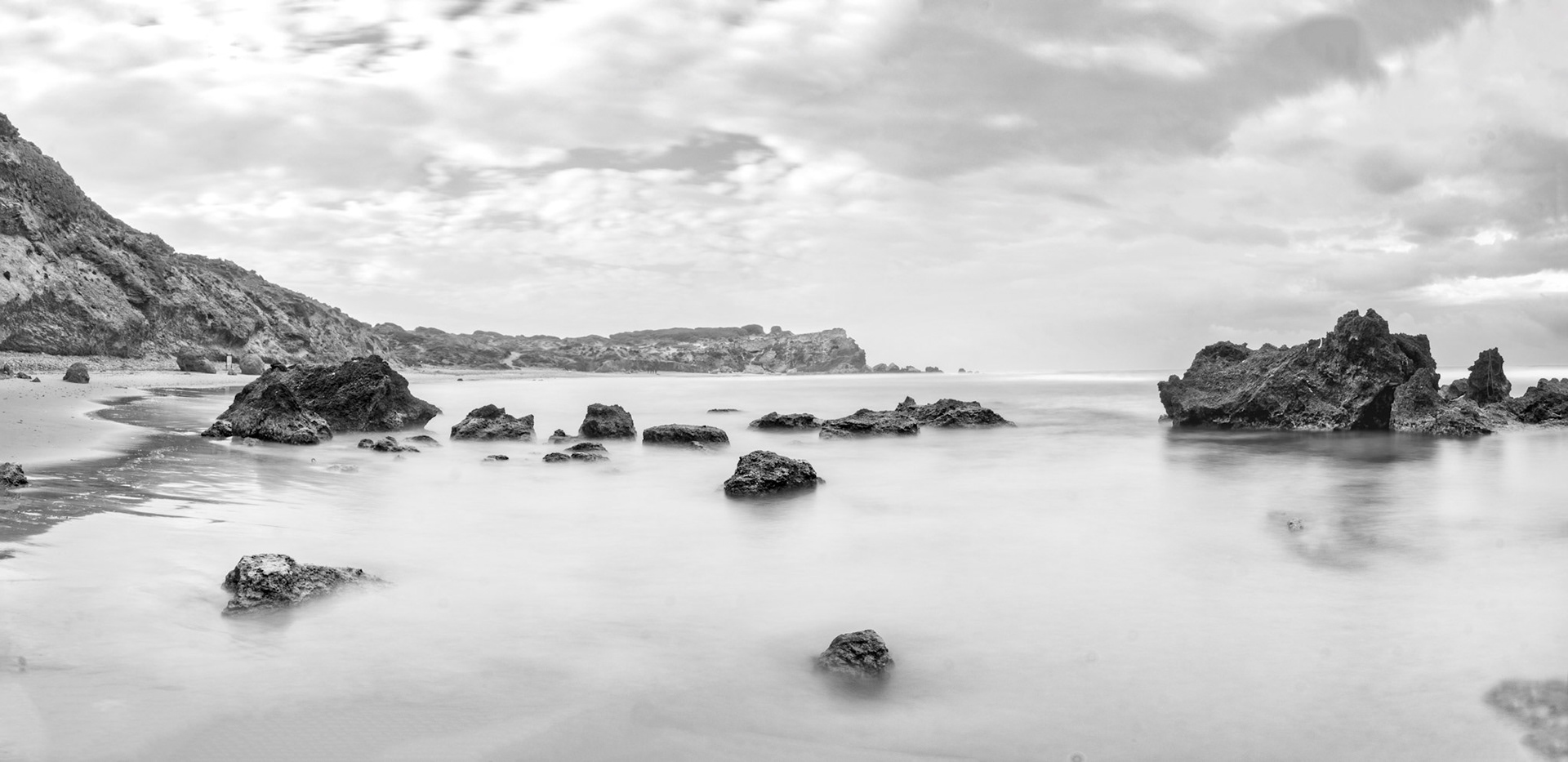 Panoramic view of Gedor national park sea reserve: group of small rocks scattering from the sand and in water toward a bigger rock inside the sea. clouds in the skies