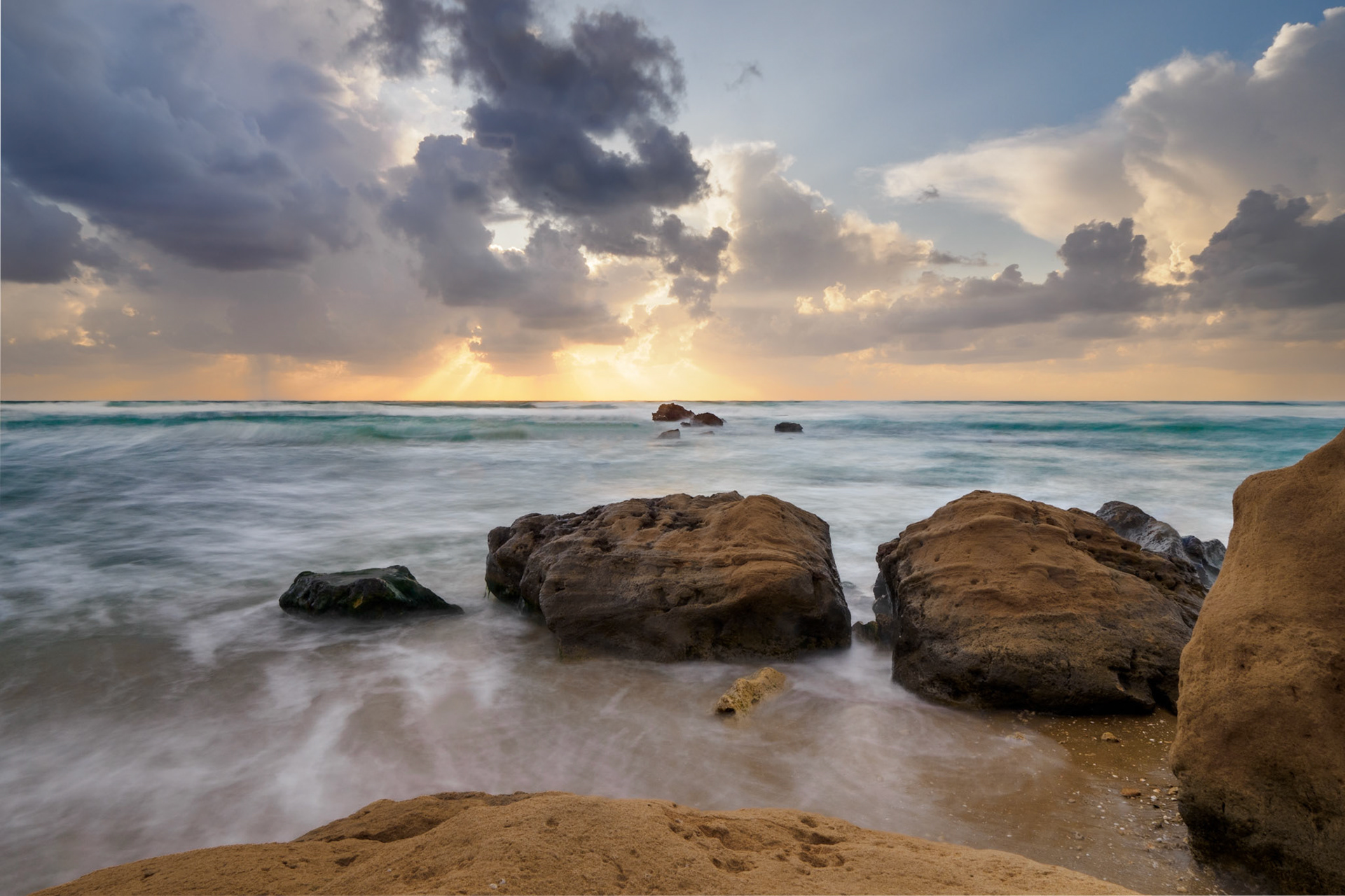 Sun rays on the sea during the sunset with rocks in the beach