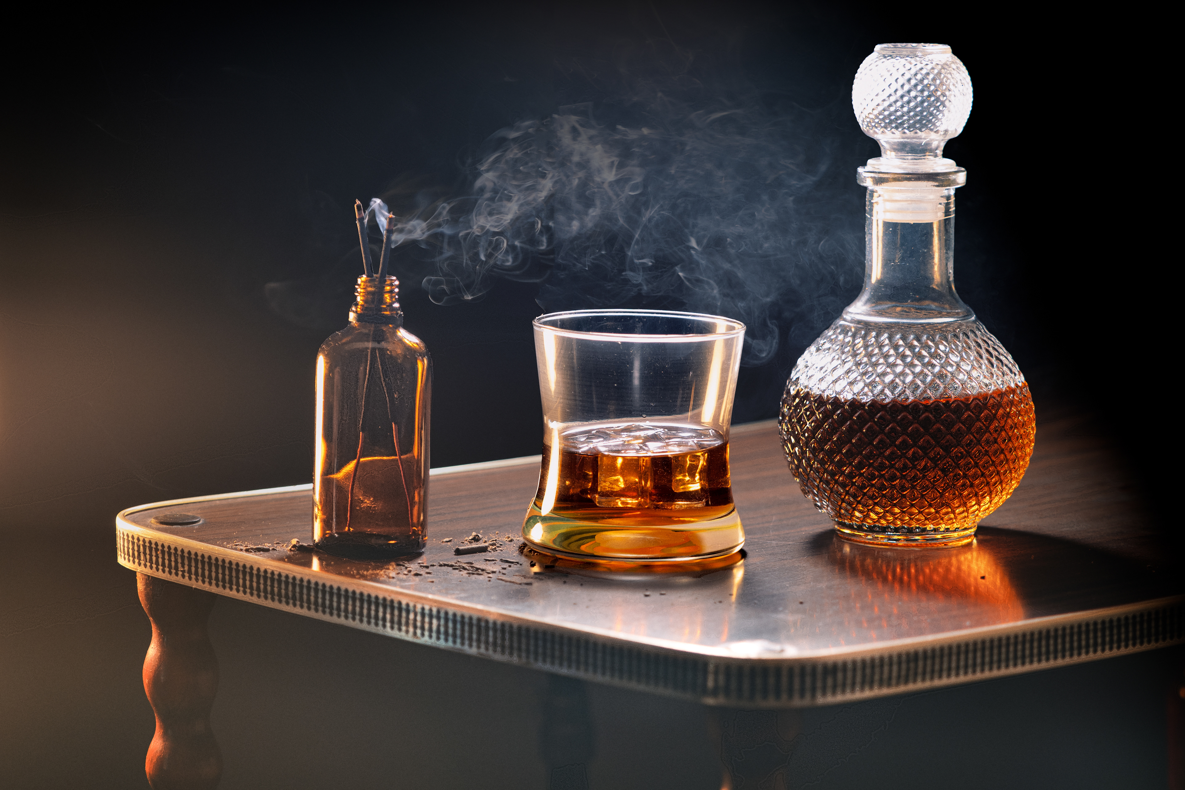 A glass of whiskey with a decorated bottle of whiskey and some incense