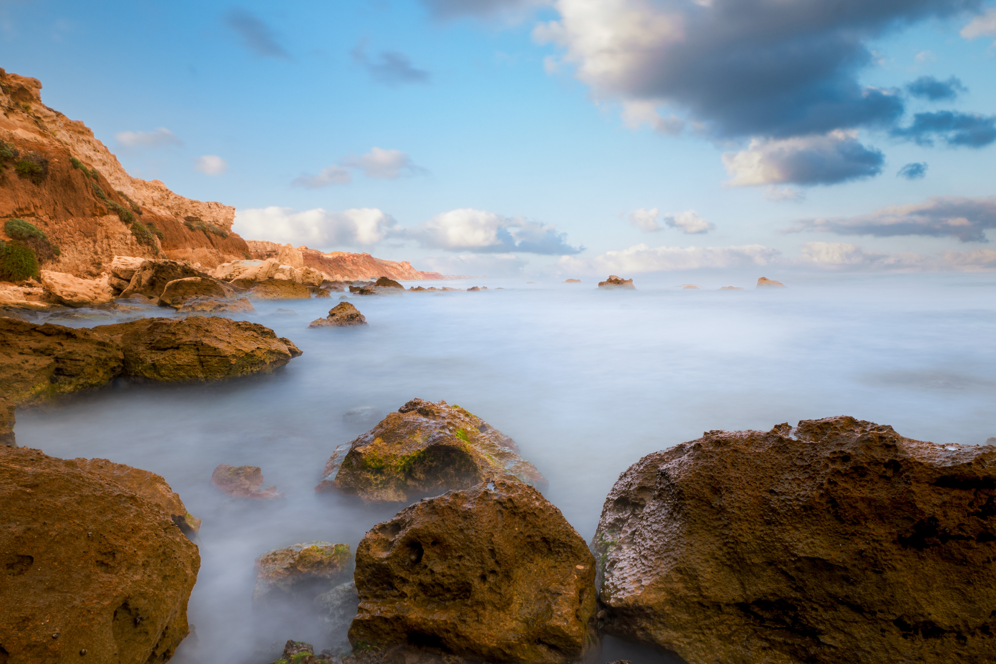 Rocks and a cliff in a long exposure shot of the beach.