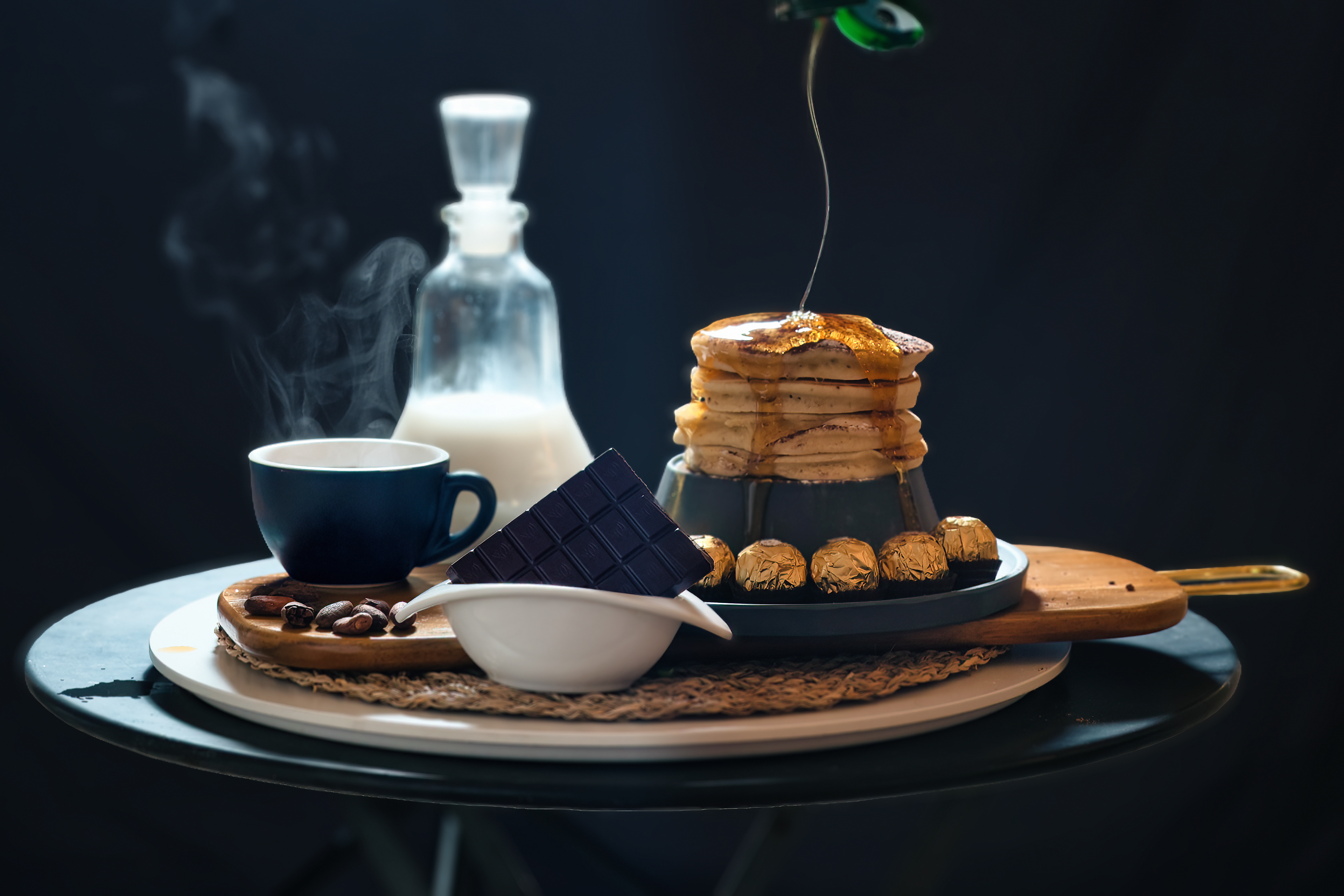 Still life with pancakes, honey, coffee, milk and dark chocolate on a wooden tray.