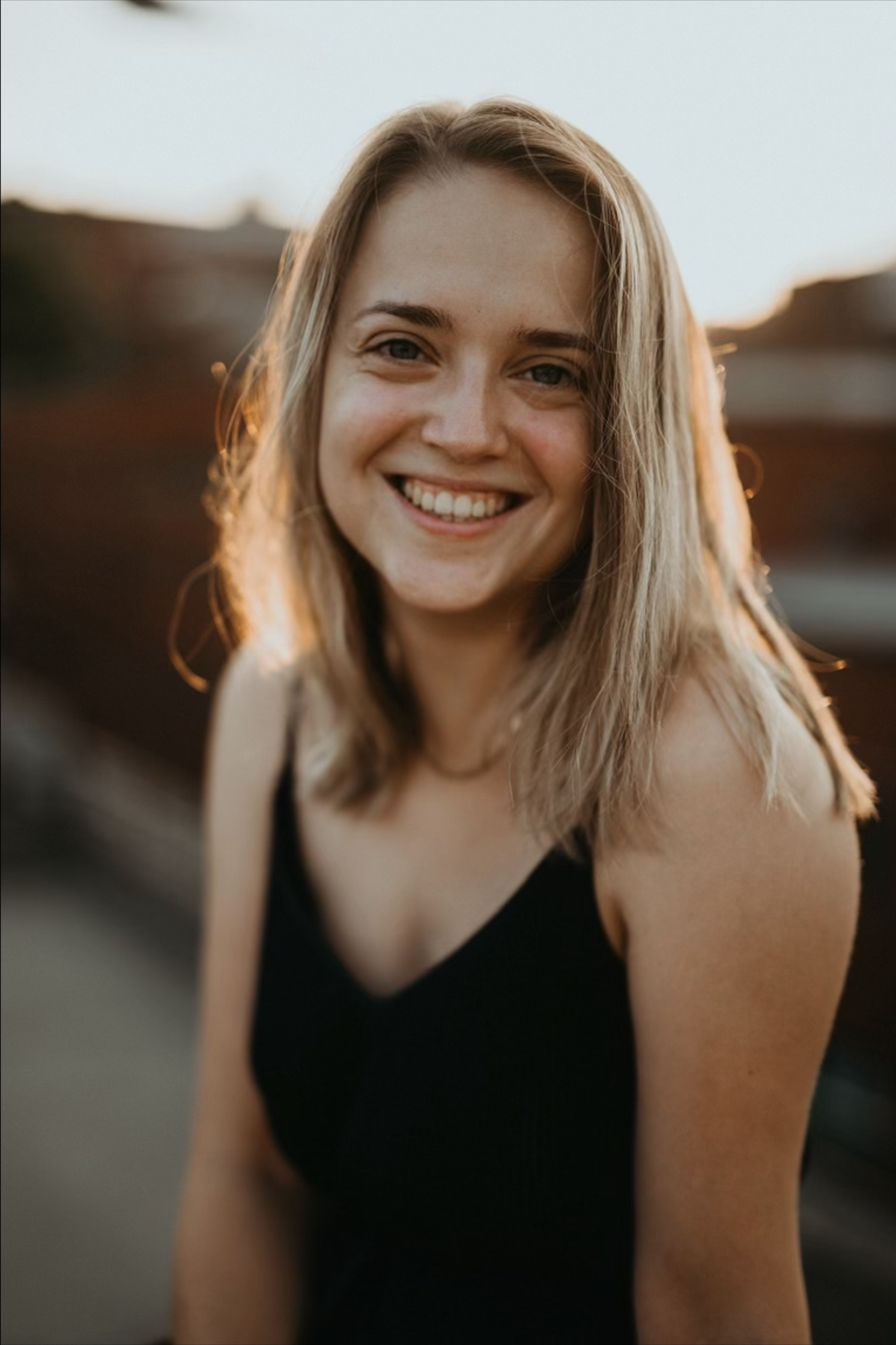 blond girl smiling at the camera, green eyes, navy dress, summer golden hour