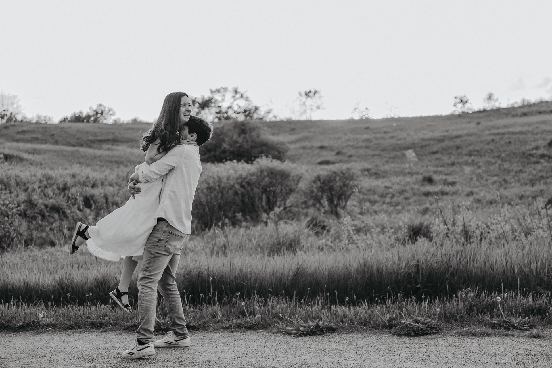 boyfriend spinning laughing girlfriend in a field, man spinning wife in a field, white dress, black and white