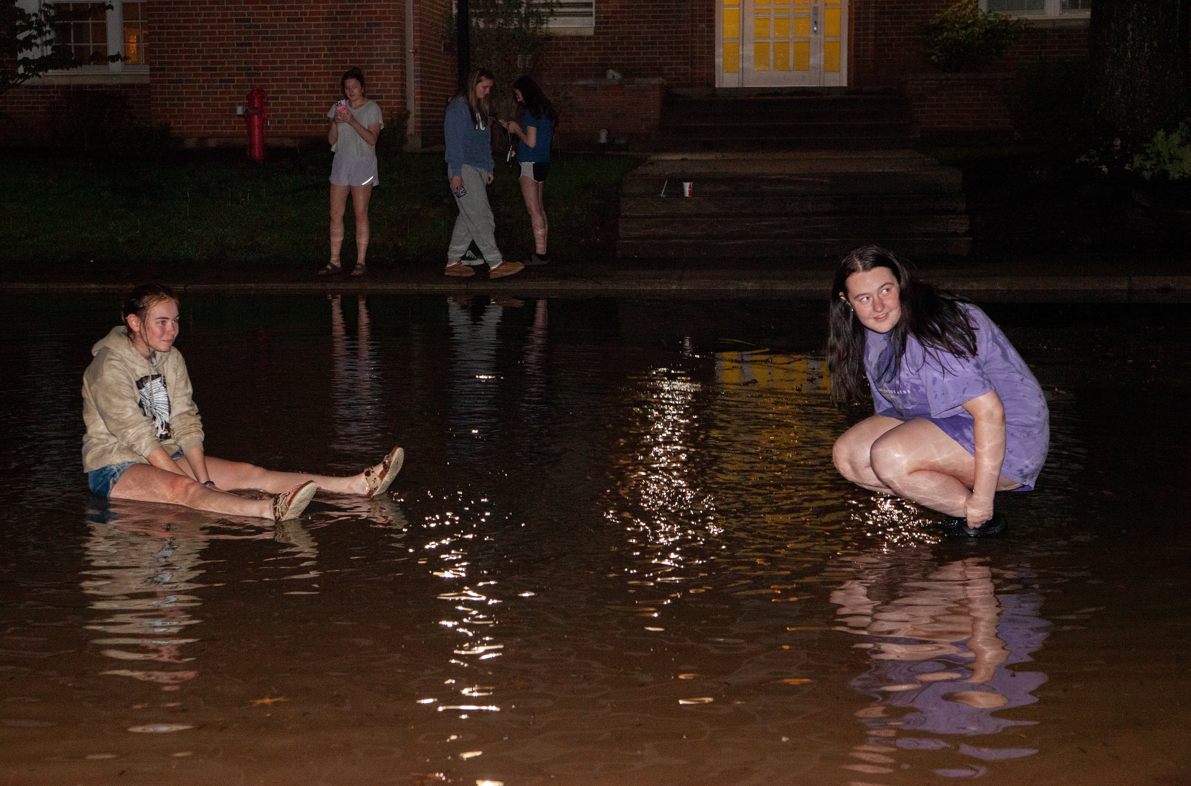 Trista Harpold (left) and Hailey Ramsey (right) play in standing water outside of Johnson hall on East Green, April 17, 2024, in Athens. The standing water is a result of the downpour of rain that happened that evening. A section of the road that separates buildings on East Green was flooded.