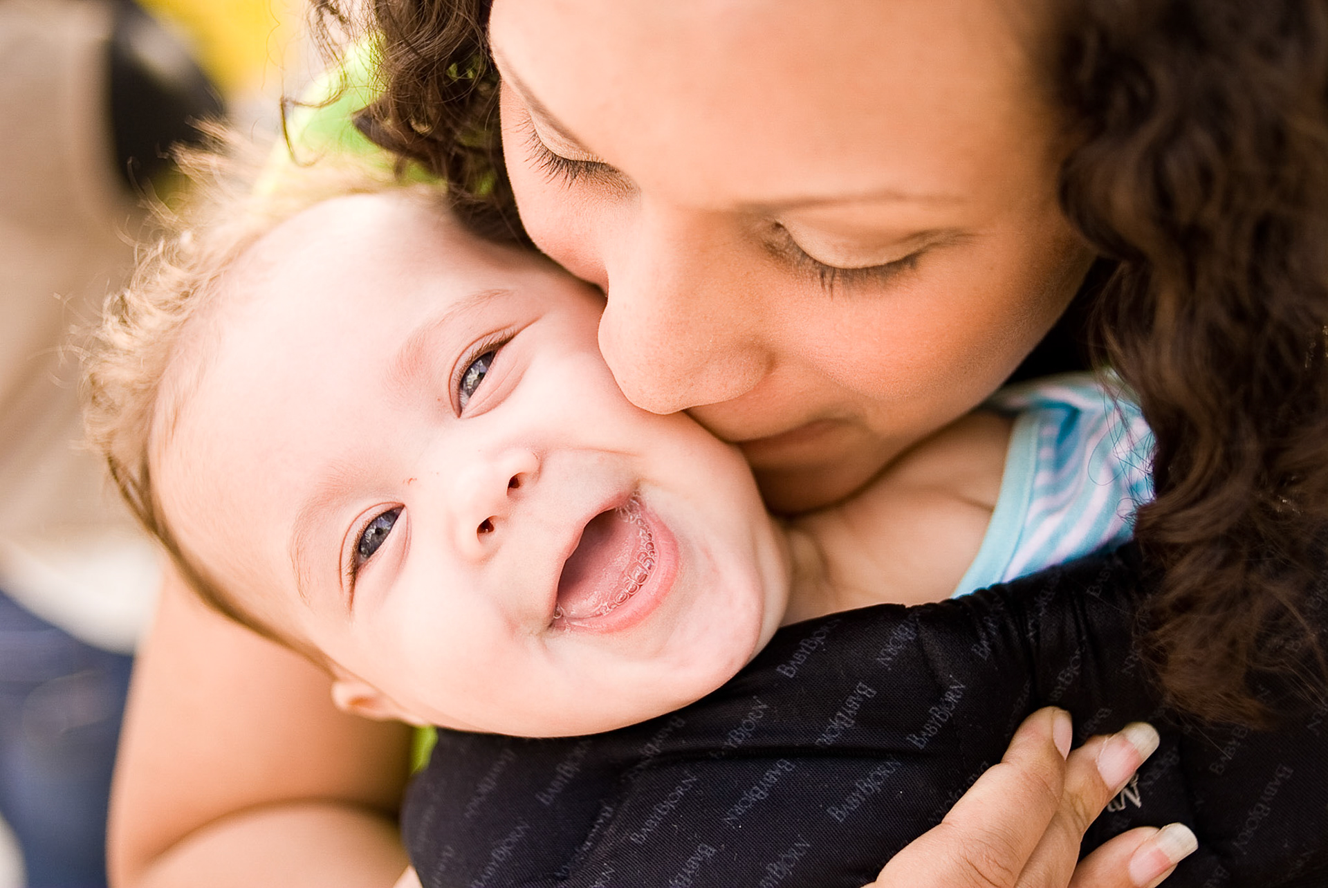 A baby girl laughs as her mom gives her kisses.