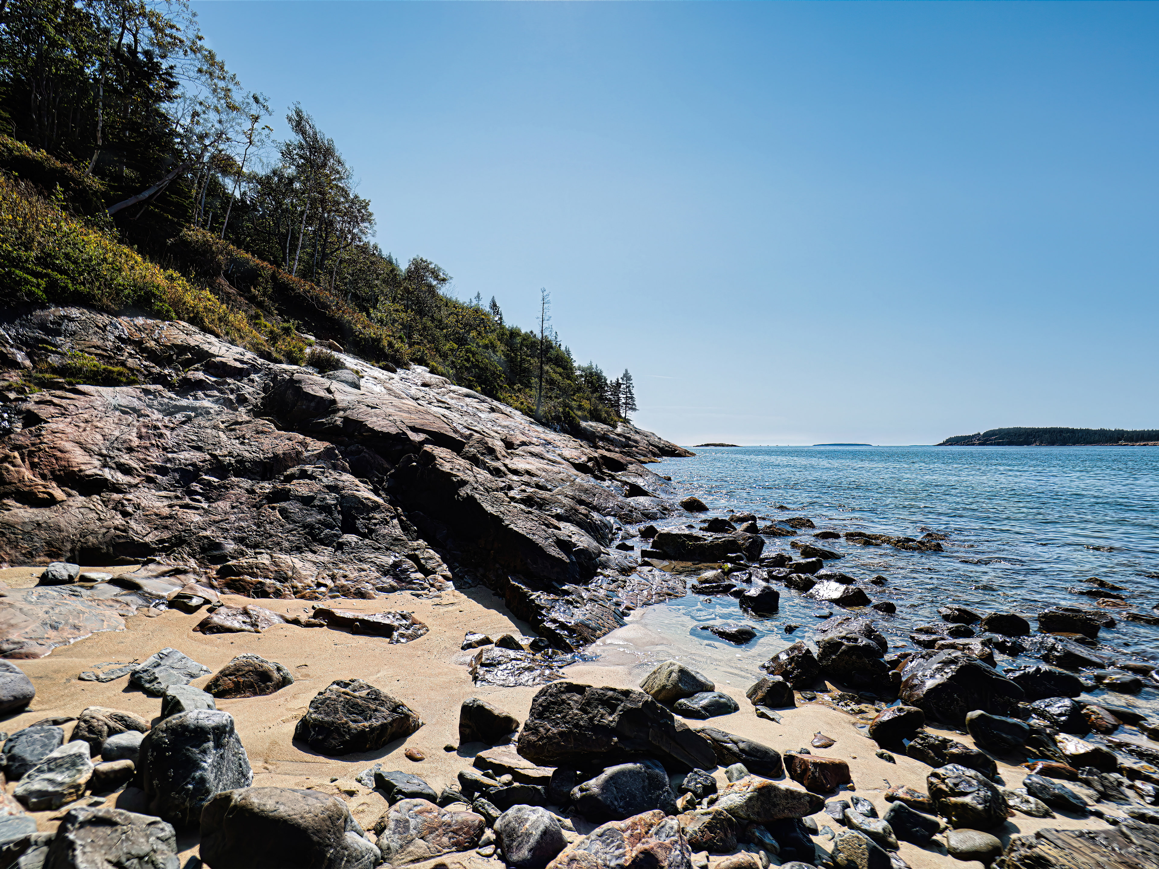 View of the rugged coastline surrounding Sand Beach in Bar Harbor, Maine, with rocky headlands framing the sandy shore and meeting the ocean.
