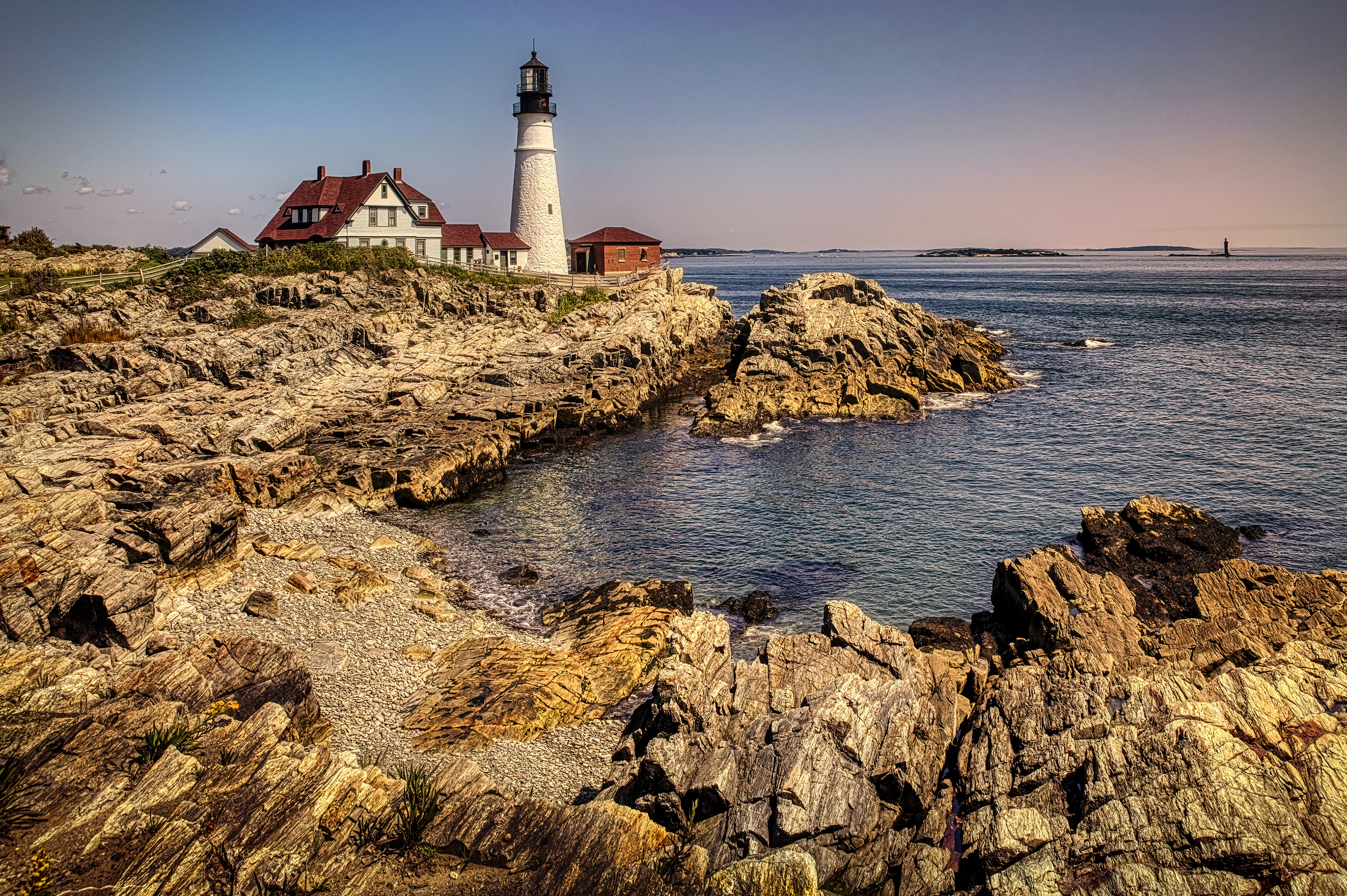 View of the rugged coastline surrounding the Portland Head Light lighthouse in Portland, Maine, showcasing the rocky shore and the Atlantic Ocean.