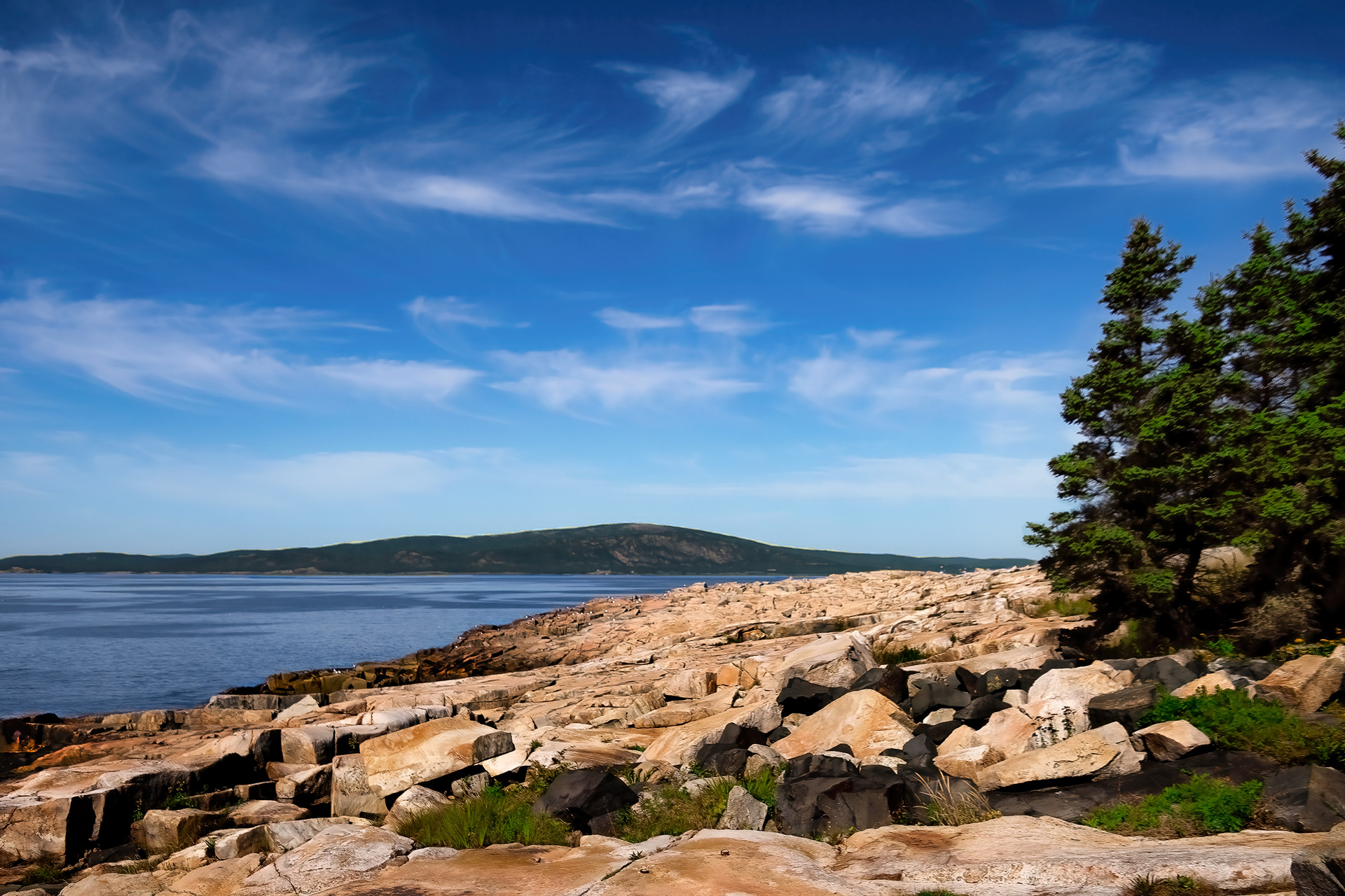View of Frazer Point in Winter Harbor, Maine, showing wispy clouds above a rugged, tree-lined coastline.