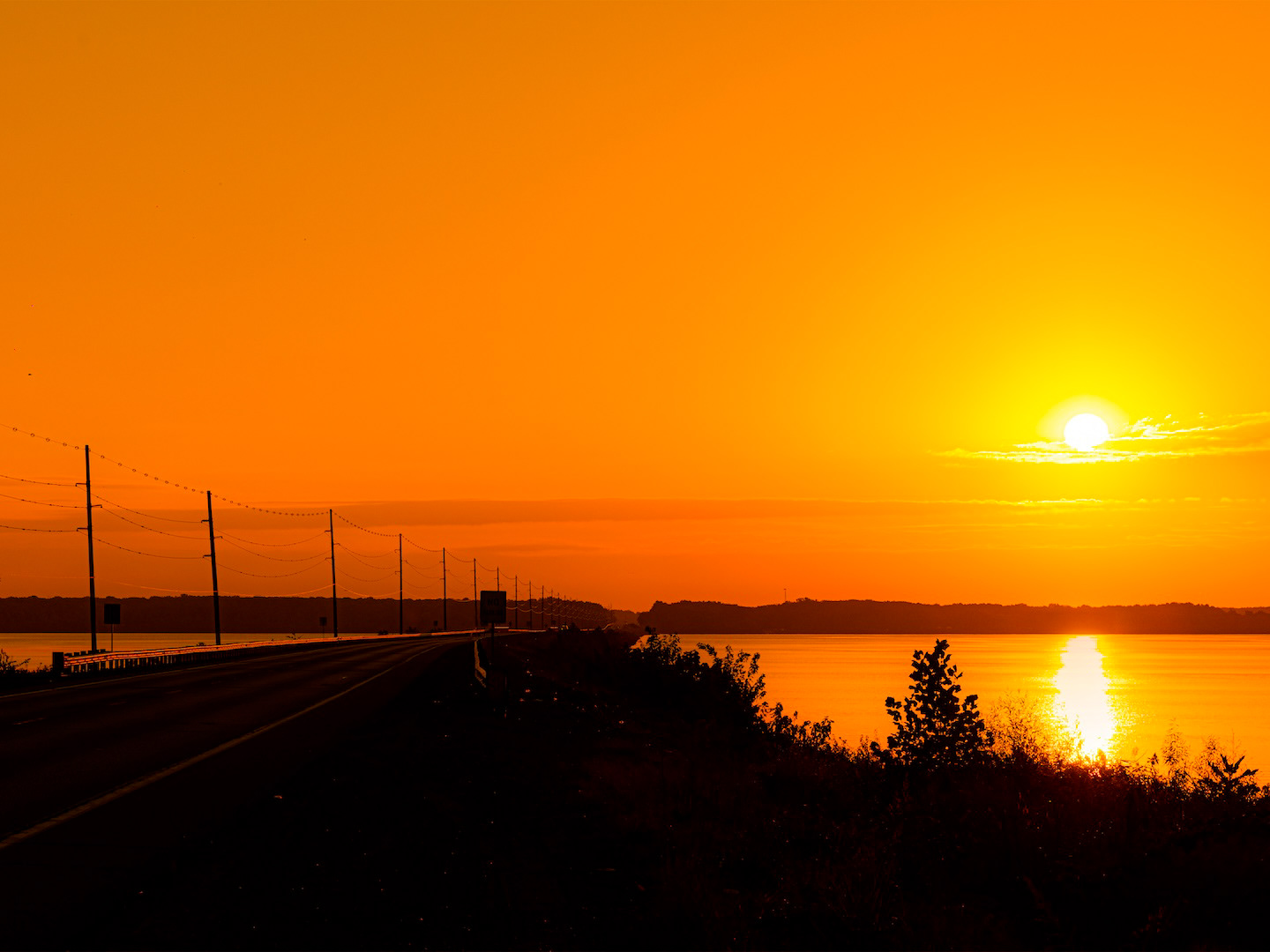 A beautiful early sunrise over Rend Lake, Illinois, likely showing vibrant colors in the sky as the sun ascends, with its light reflecting on the calm lake waters and silhouetting the shoreline.