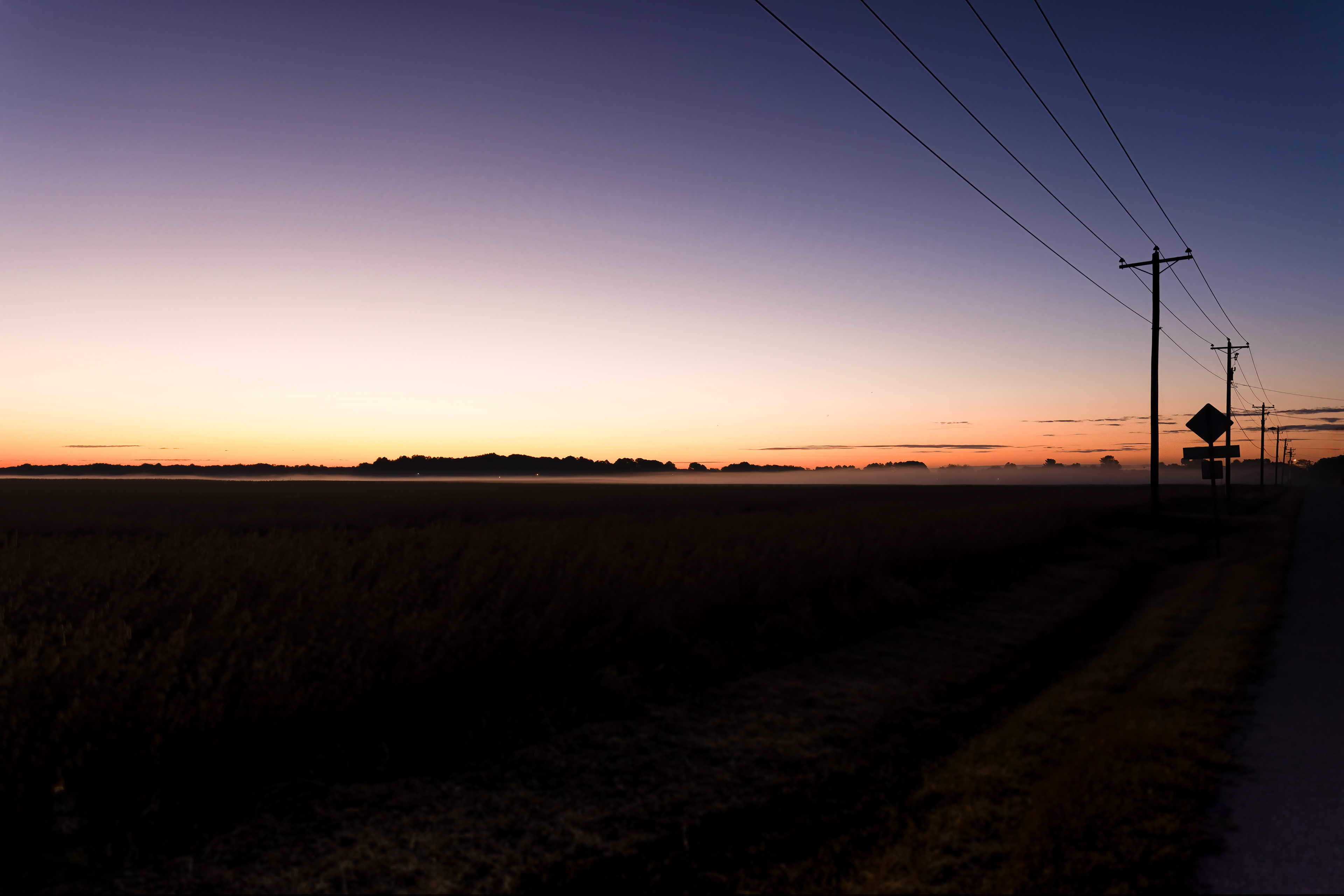 An early sunrise morning, with the light laced with fog, illuminates a distant farmer's field on the Eastern Shore of Maryland.