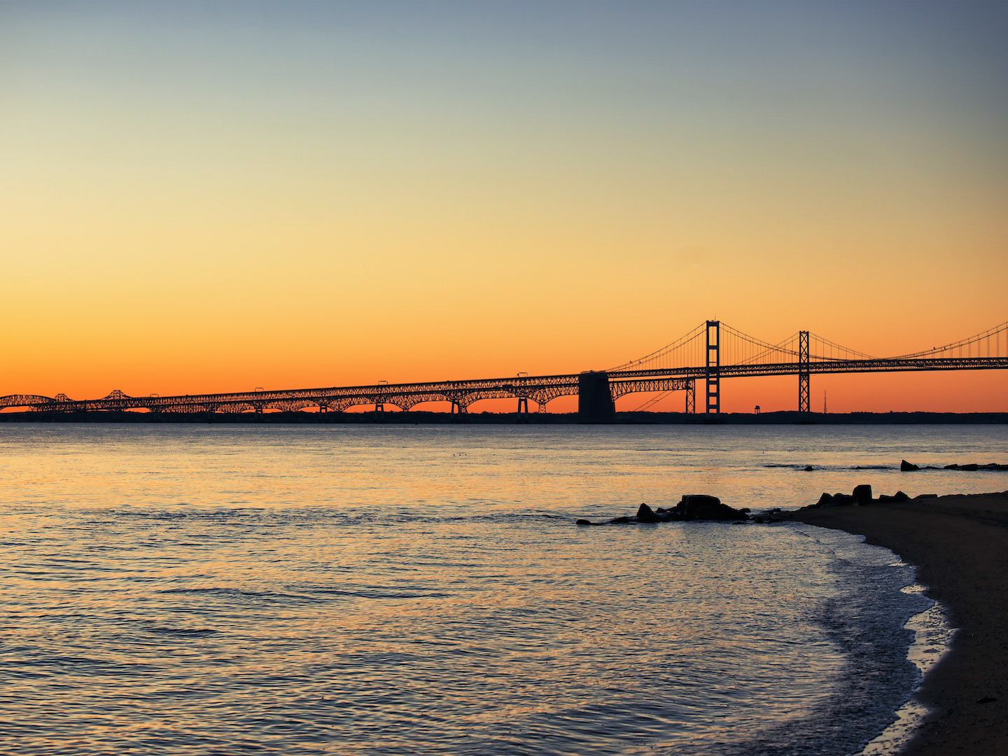 Scenic beach with a distant bridge under clear blue skies.
