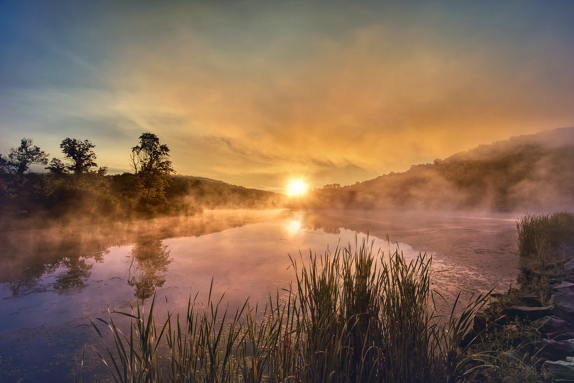 A beautiful sunrise peaks through the morning fog over Keystone Lake at Keystone State Park, Pennsylvania.