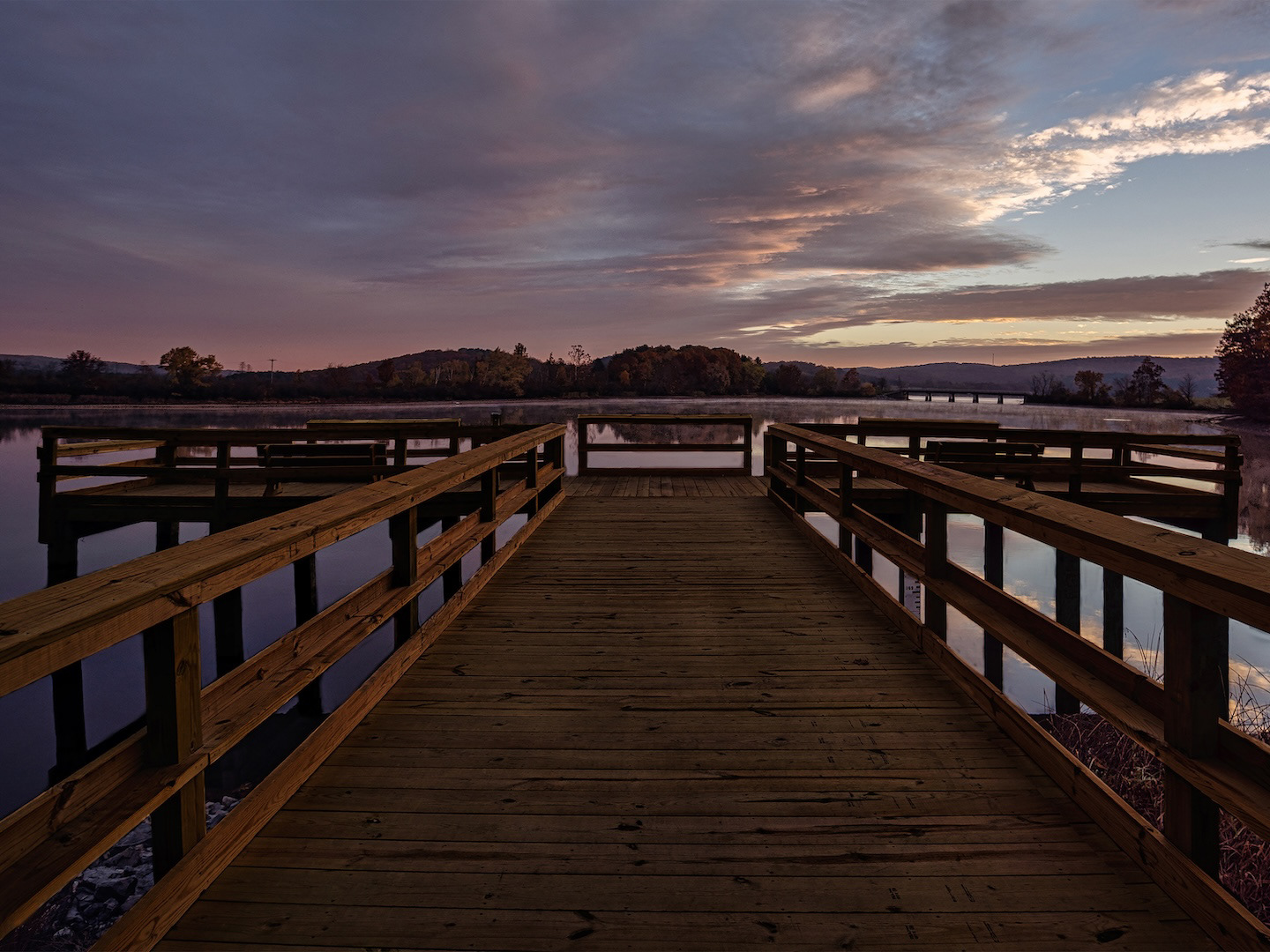 Scenic wooden pier over peaceful water, with trees reflecting in the river.