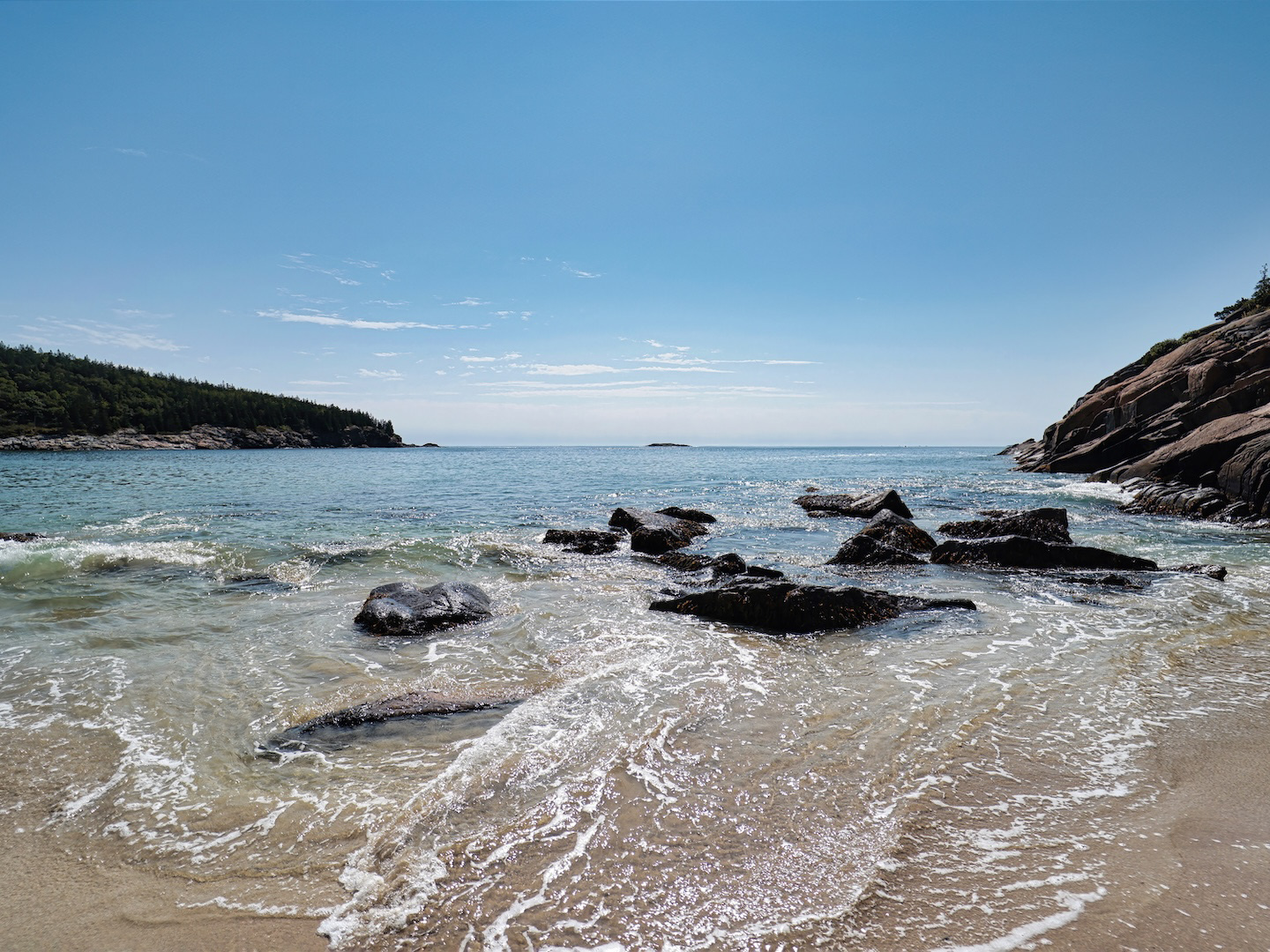 View of swirling waves and the rugged coastline surrounding Sand Beach in Bar Harbor, Maine, showing the dynamic ocean meeting the rocky headlands and sandy shore.