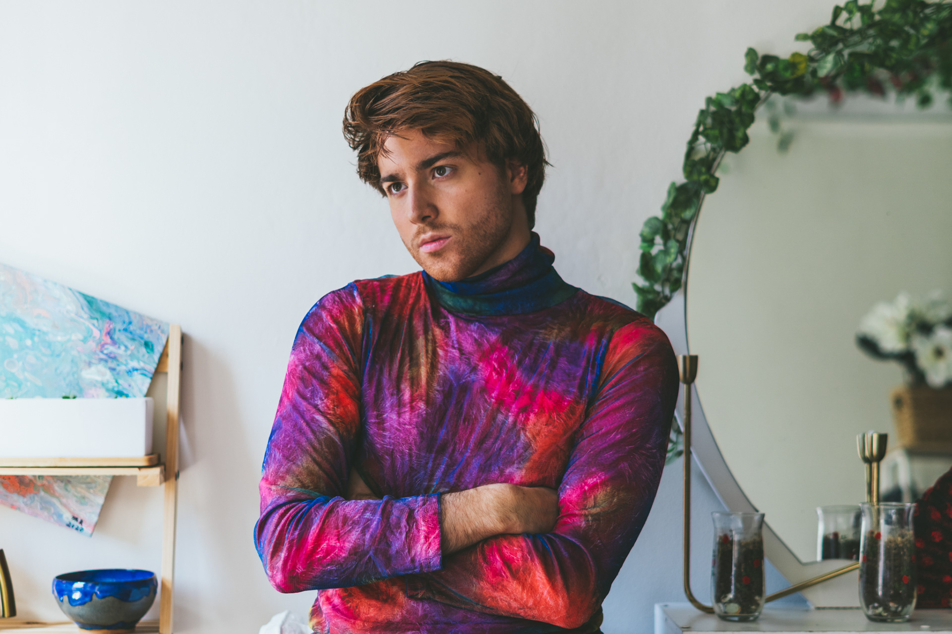 Zac Wichlei, interdisciplinary creative and researcher, standing indoors in a colourful turtleneck, looking thoughtfully into the distance.