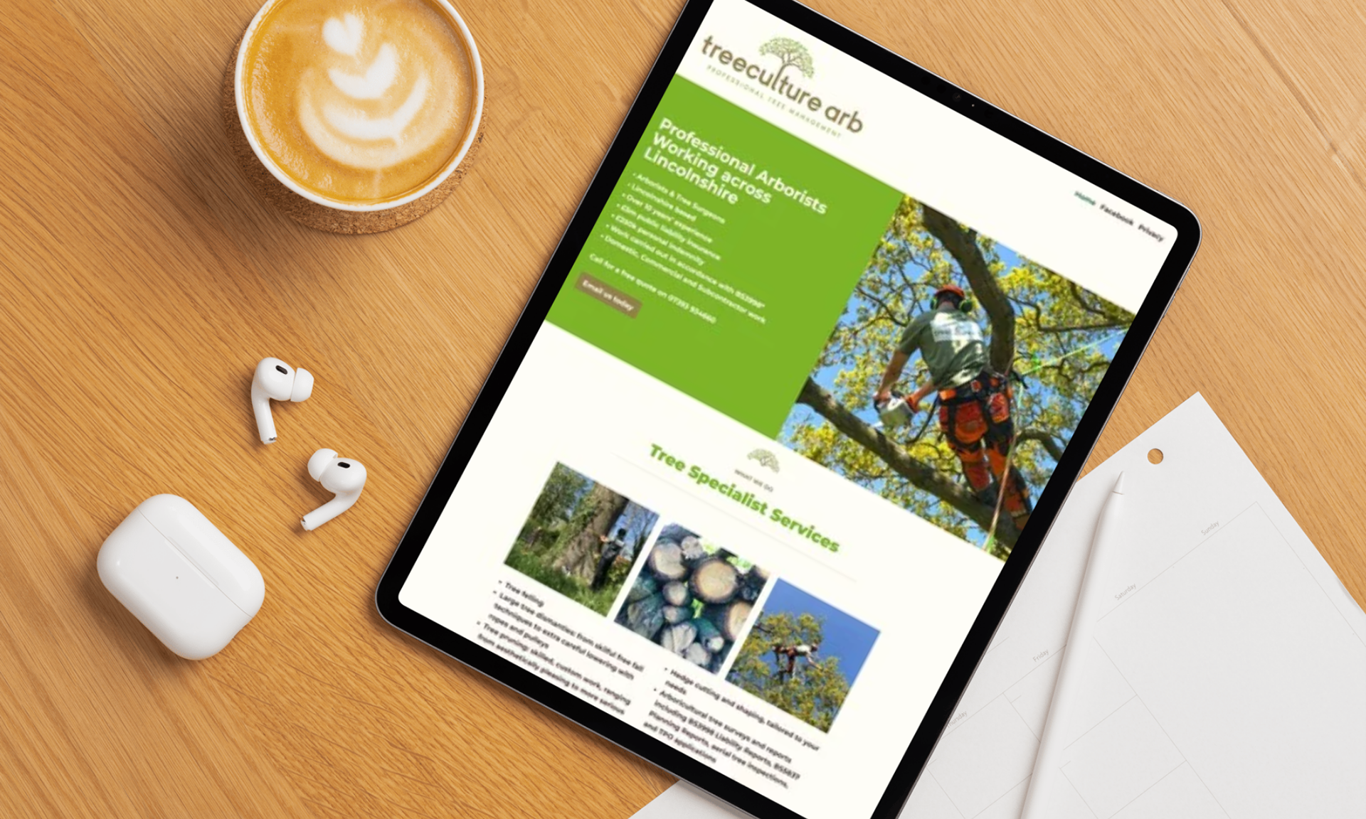 Tablet showing the homepage of Treeculutre Arb (tree surgeons), with coffee, AirPods and note paper