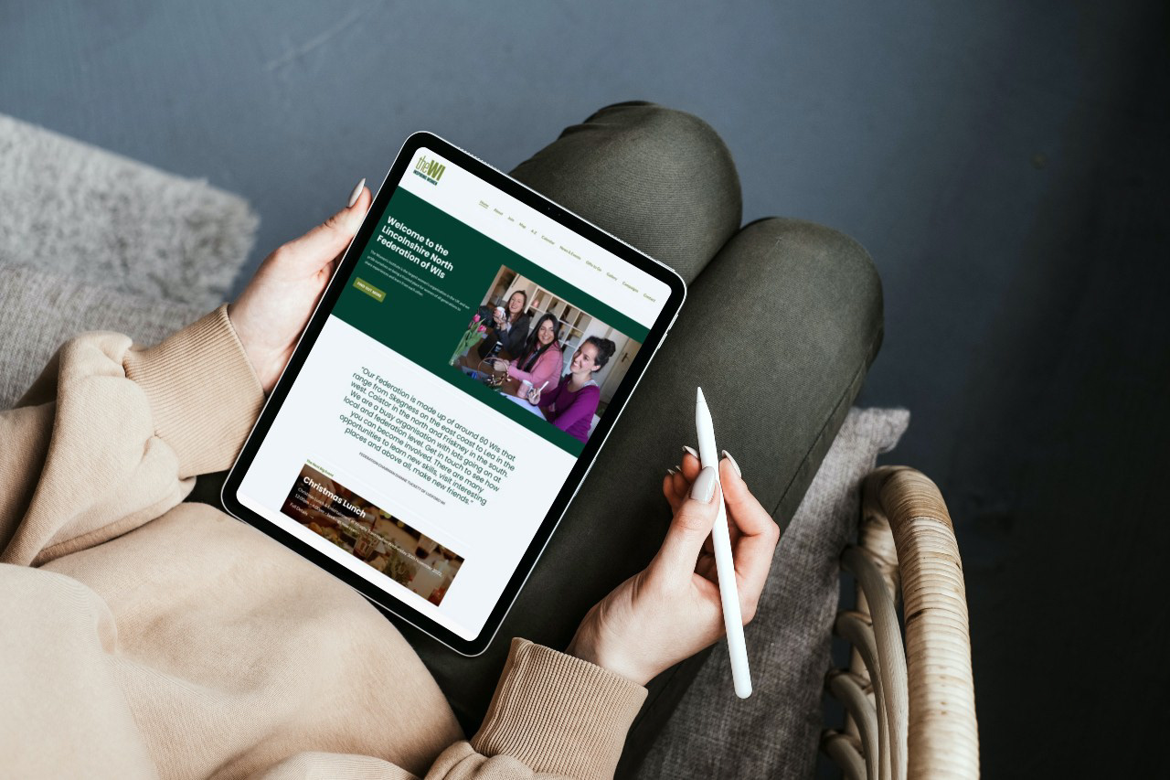 Website displayed on a tablet perched on a woman's knee, showing the home page for Lincolnshire North Women's Institute