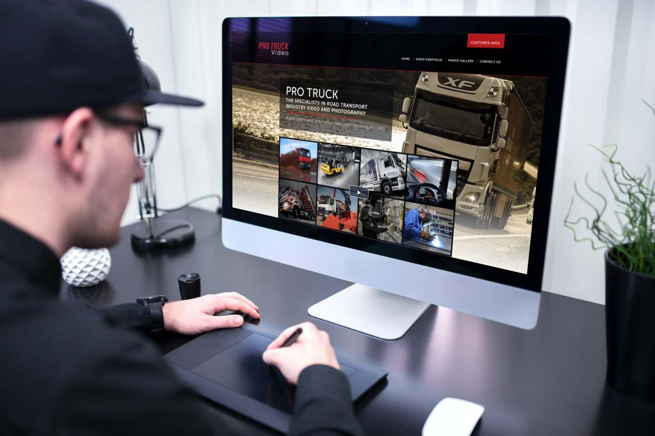 A man is looking at a large Mac monitor showing the homepage for Pro-Truck-Video. He is working with a tablet.