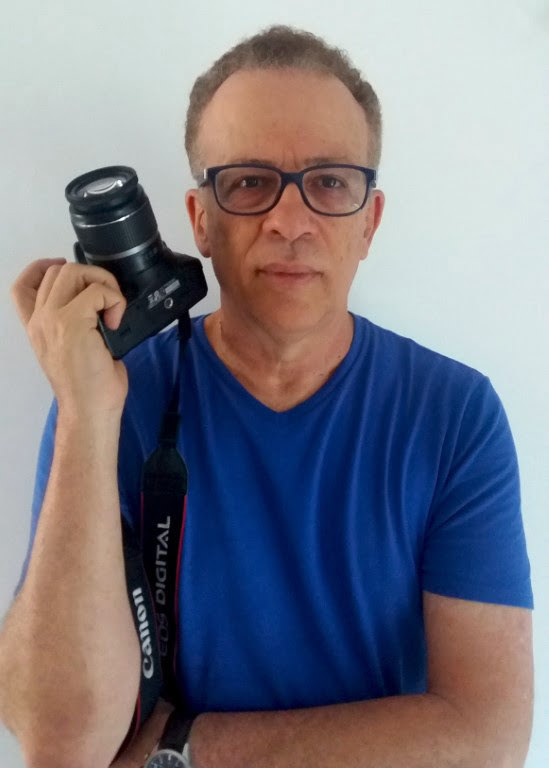 Delson usando uma camiseta azul e segurando a câmera fotográfica com a mão