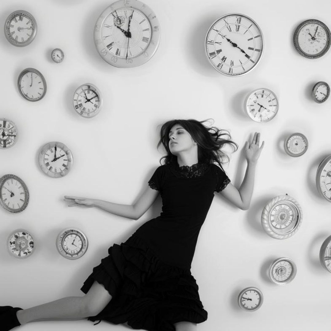 Create a lady, laying down, floating clocks, spiral, dreamlike, white background, photography larry clar.