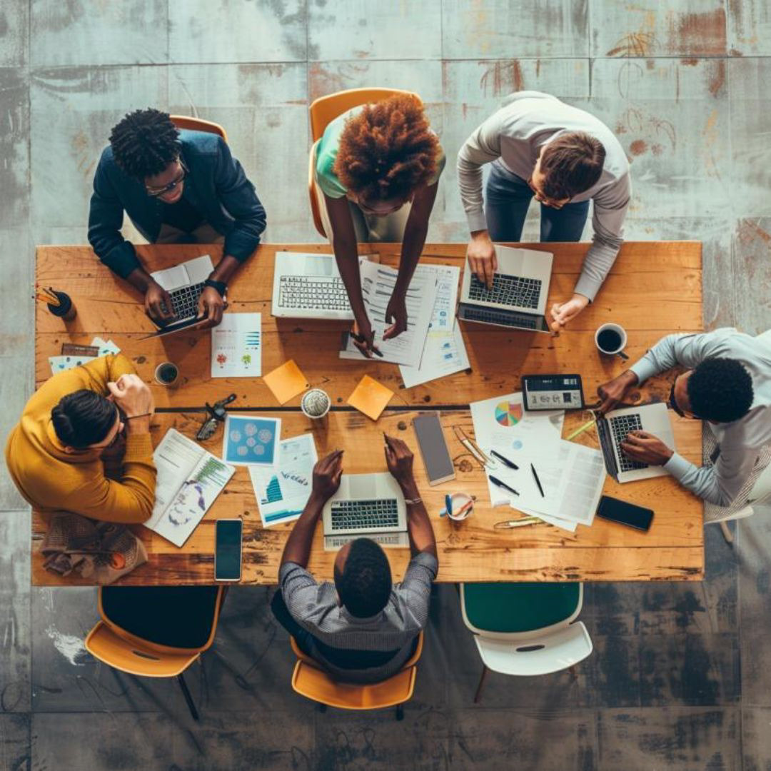 Create a realistic image of a diverse team of coworkers gathered around a table brainstorming ideas, top view.