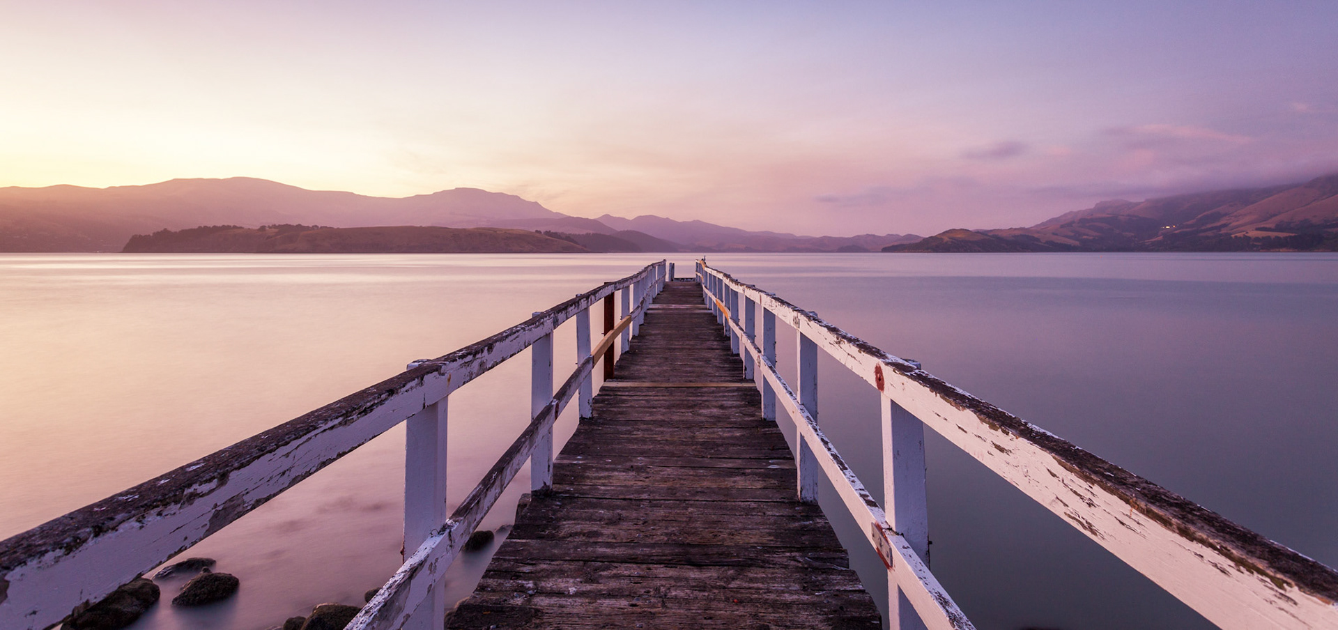A serene soft light of sunrise looking out over a jetty in Lyttelton Harbour