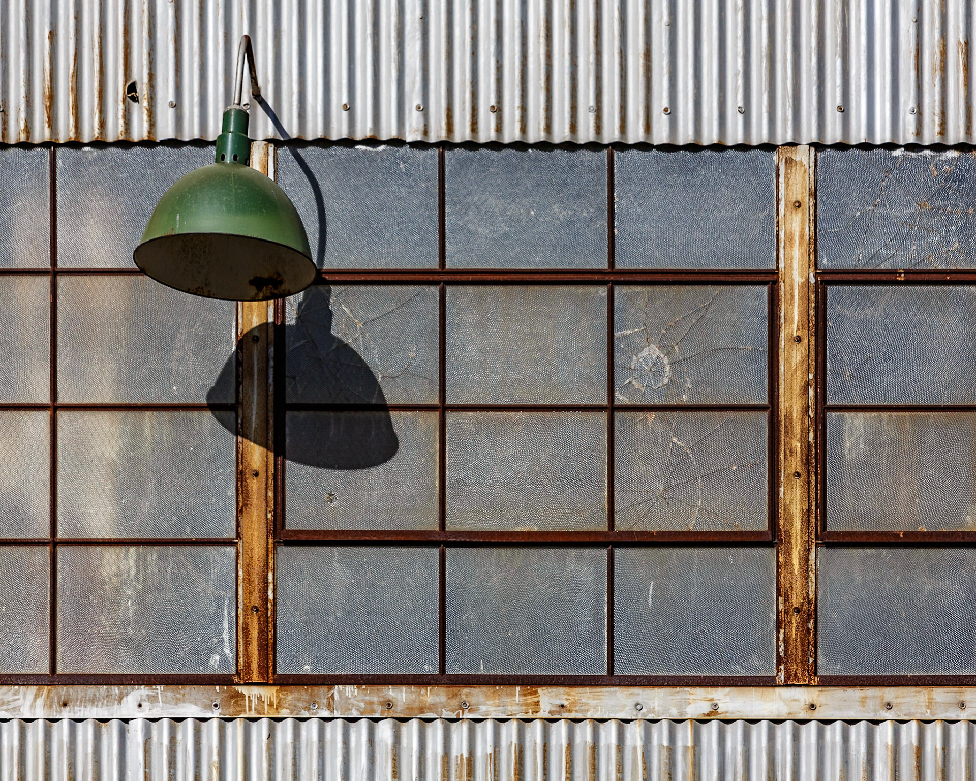 Lampara de metal en una pared de metal corroído con una hilera de ventanas de cristal.