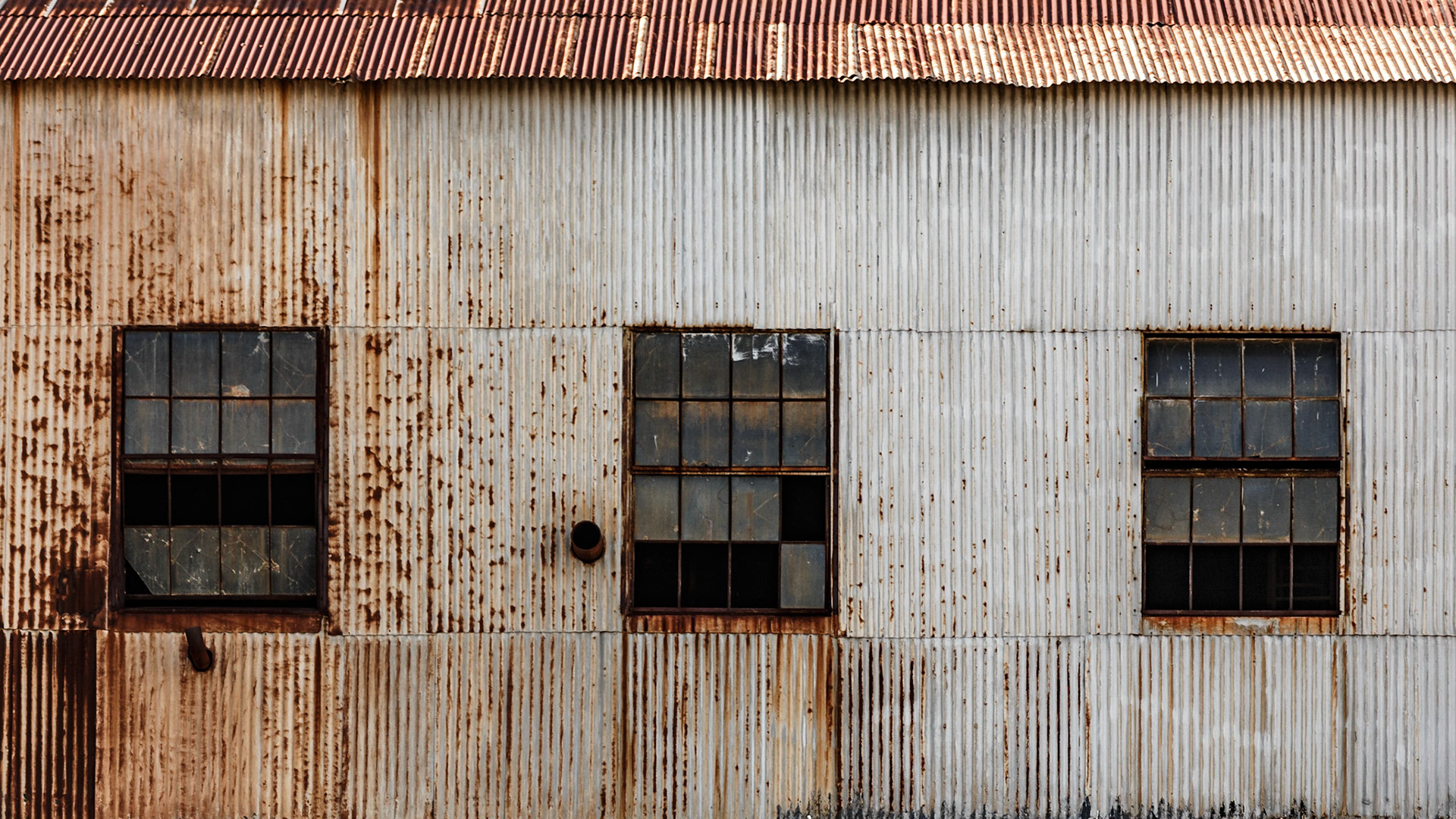 Pared de metal con tres ventanas de cristal rotas.