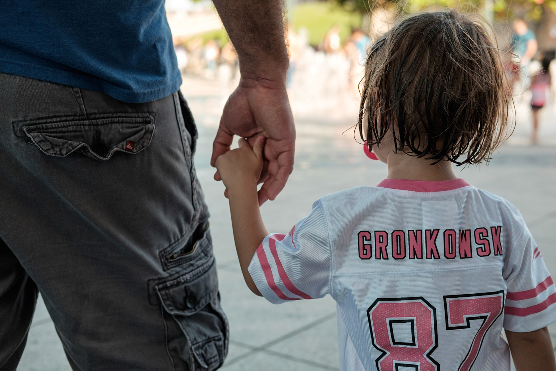 Vista de espaldas de un padre agarrando la mano de su hija.