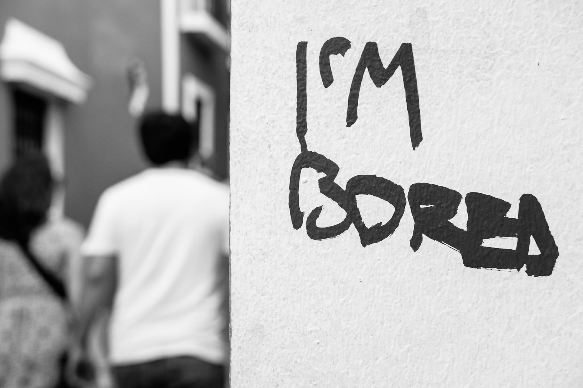 Pared escrita a la orilla de un callejón del Viejo San Juan, por donde caminan dos personas.