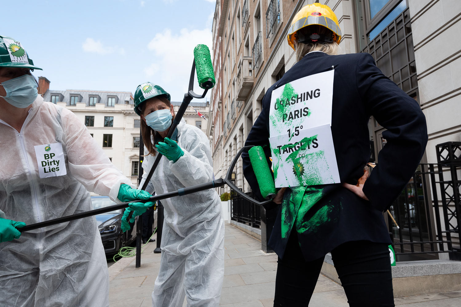 Two women dressed as decorators apply green paint to another dressed as an oil executive outside the HQ of oil company BP