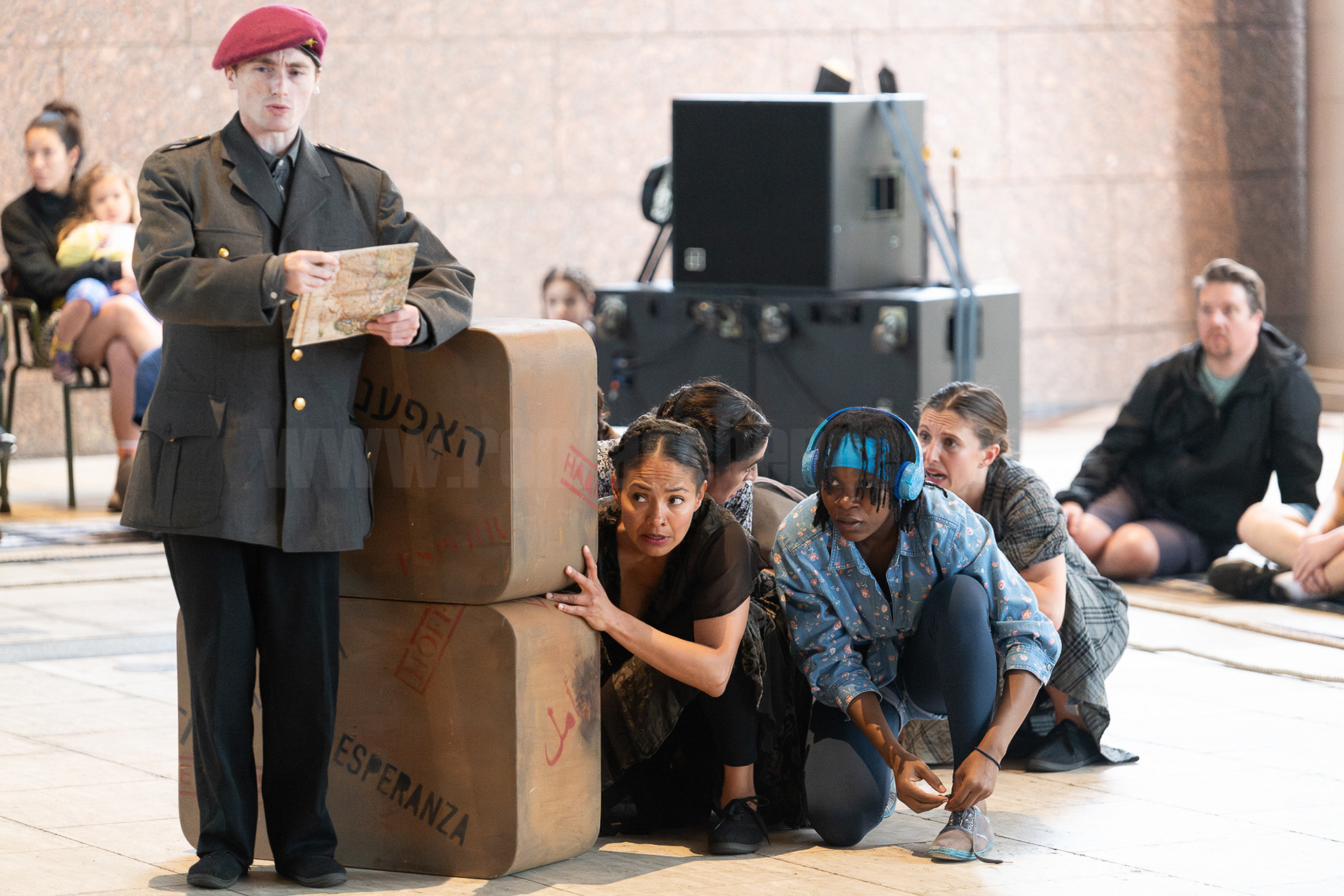 Refugees cower behind suitcases in a scene from the play "From Here On".