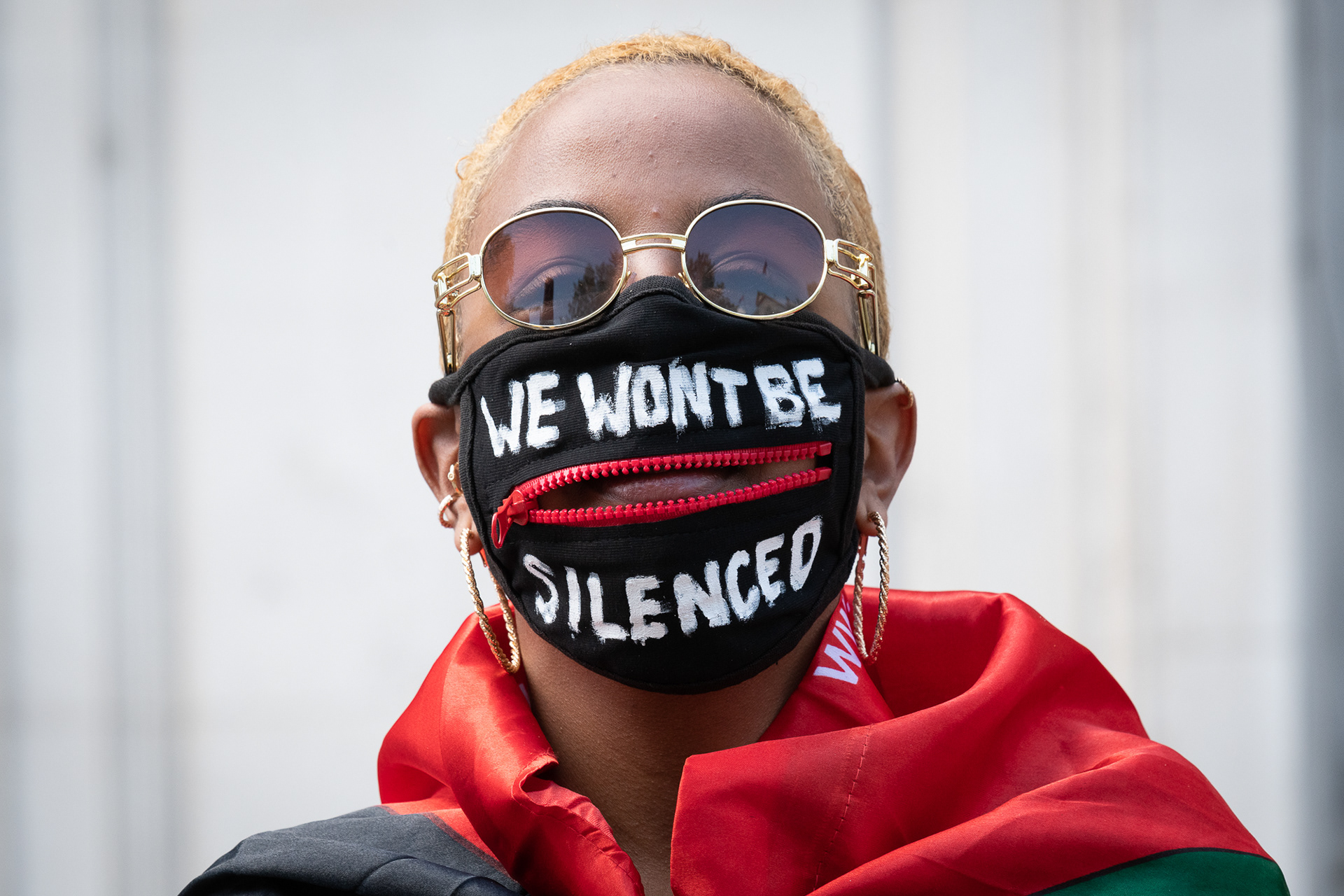 A protester wears a face mask with an open zip and the slogan "We Won't Be Silenced"
