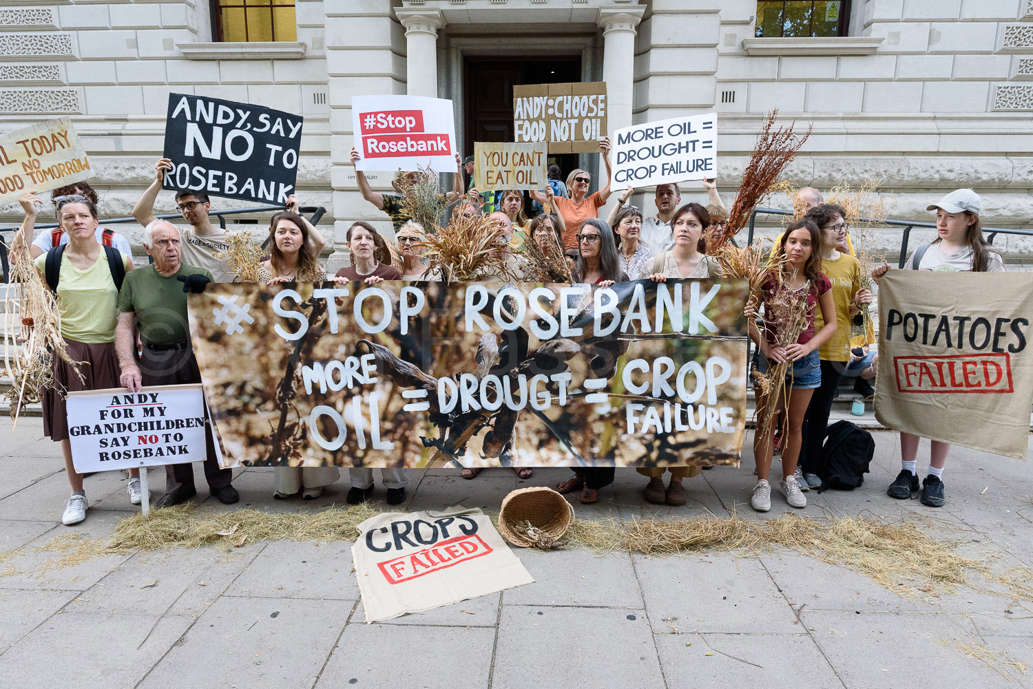 Climate activists holding withered plants stand with a banner saying "Stop Rosebank" outside HIM Treasury