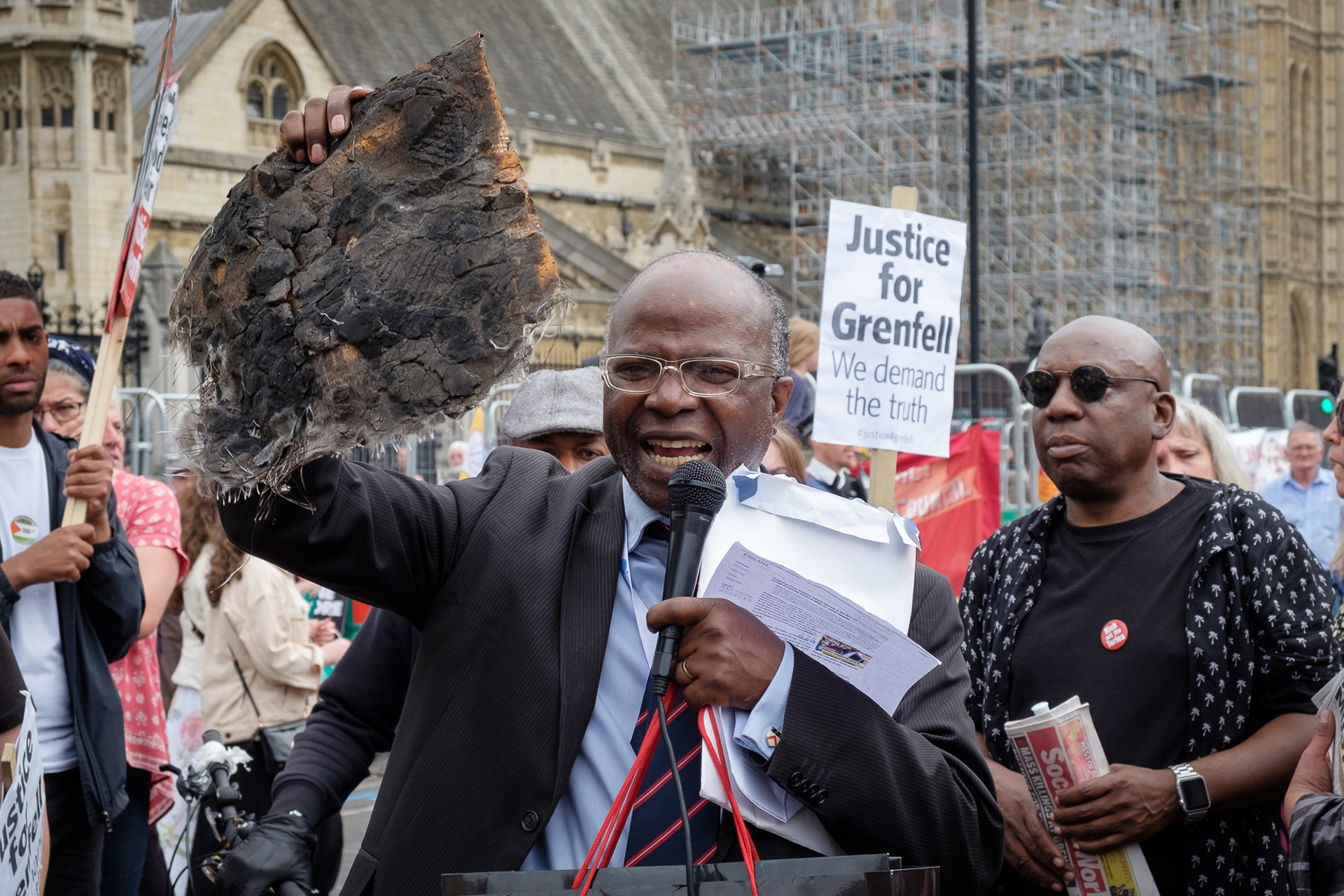 A Grenfell Tower Survivors Group supporter speaks at a rally outside Parliament holding a piece of burnt cladding found on the site of the catastrophic fire in which 72 residents died. © Ron Fassbender