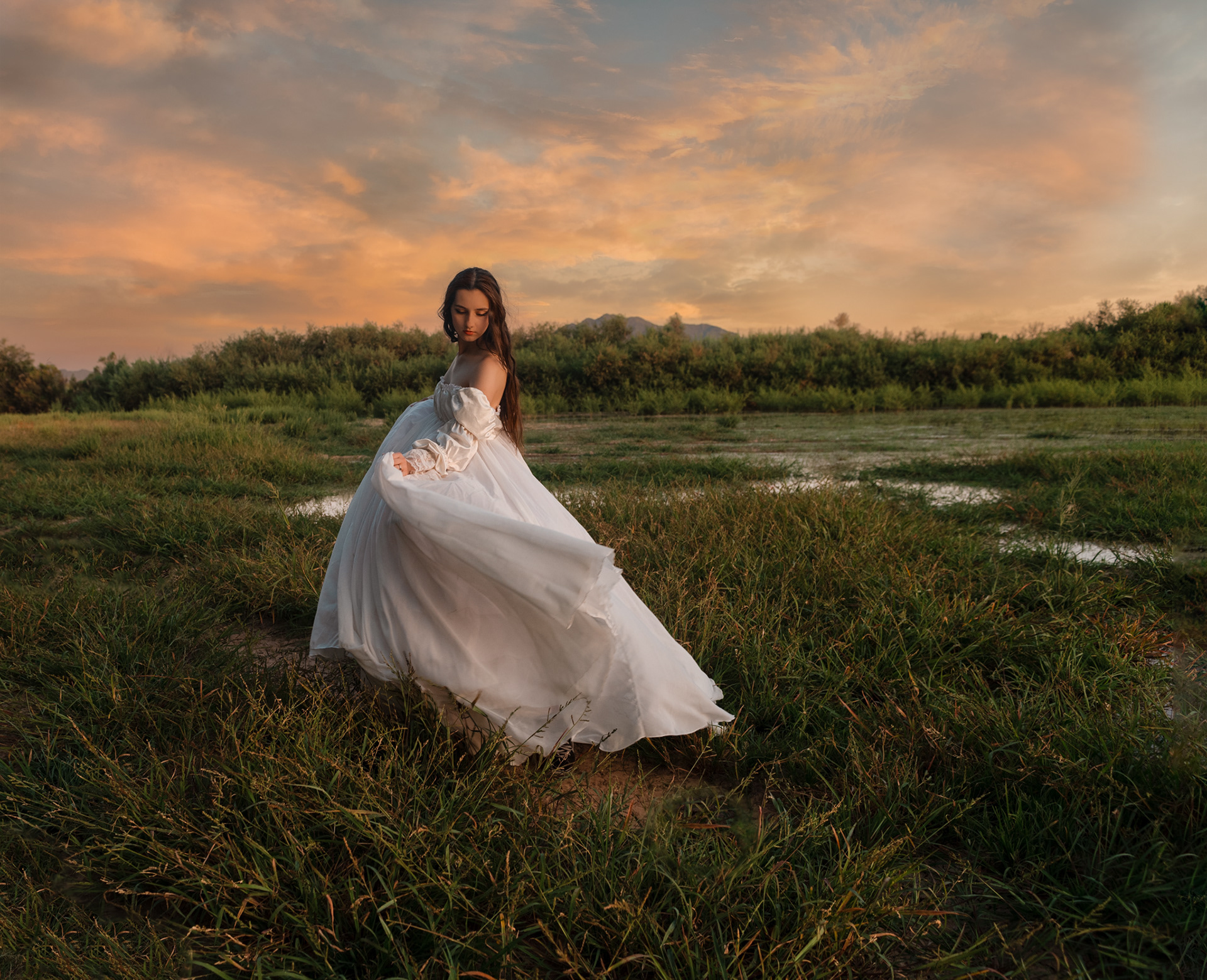 Woman in flowing white dress walking through grassy wetland at sunset, cinematic editorial portrait