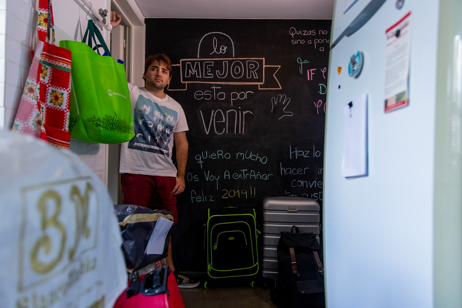 In this April 2, 2019, photo, Tomás Ruiz, 27, poses for a photo in front of a chalkboard reading ¨the best is yet to come¨ and ¨ I Love you very much, i´m gonna miss you, happy 2019¨,in his mother´s house in the City of Buenos Aires, Argentina. Before moving to Dublin, Ireland in search of work.