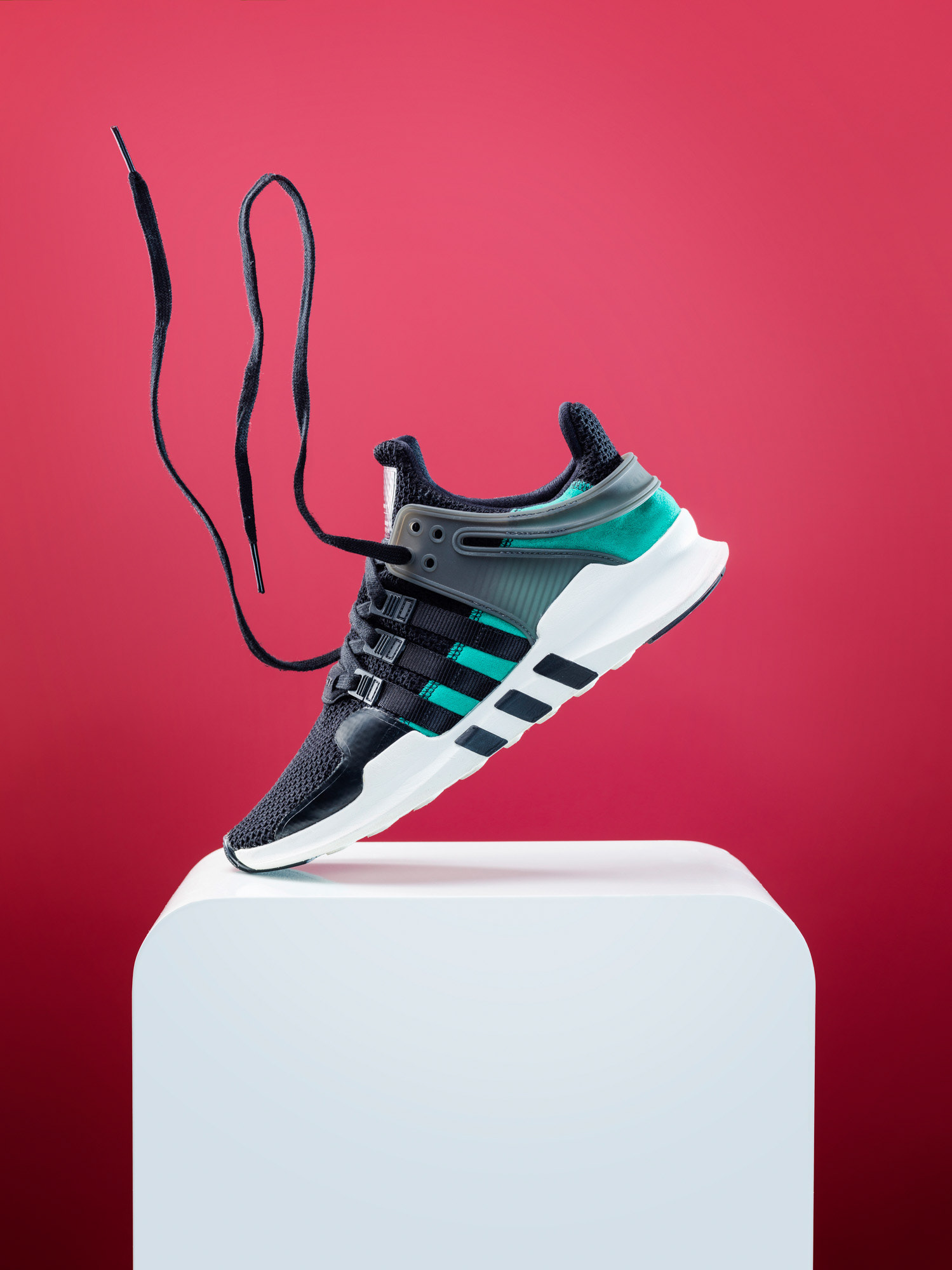 Einzelner Schuh steht nur mit der Spitze auf weißem Tische vor farbigem Hintergrund, Schnürsenkel schweben in der Luft